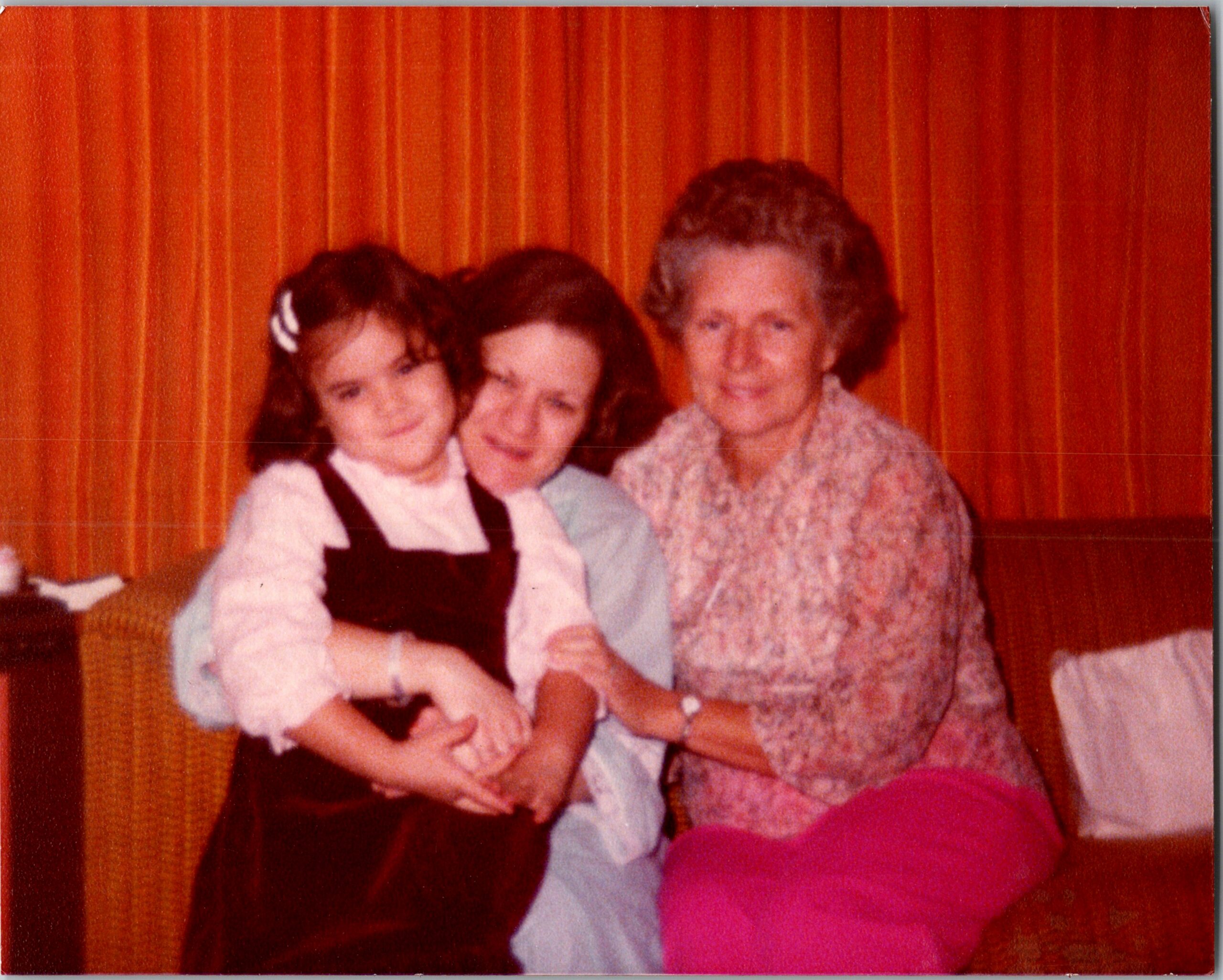 Three people posing together for a photo, two adults and a child, smiling in front of orange curtains.