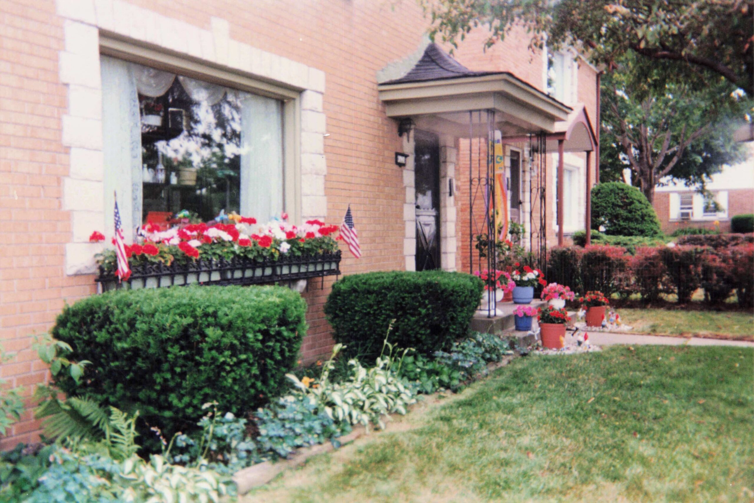 Brick building storefront with flower boxes, American flags, and manicured shrubs along the walkway.