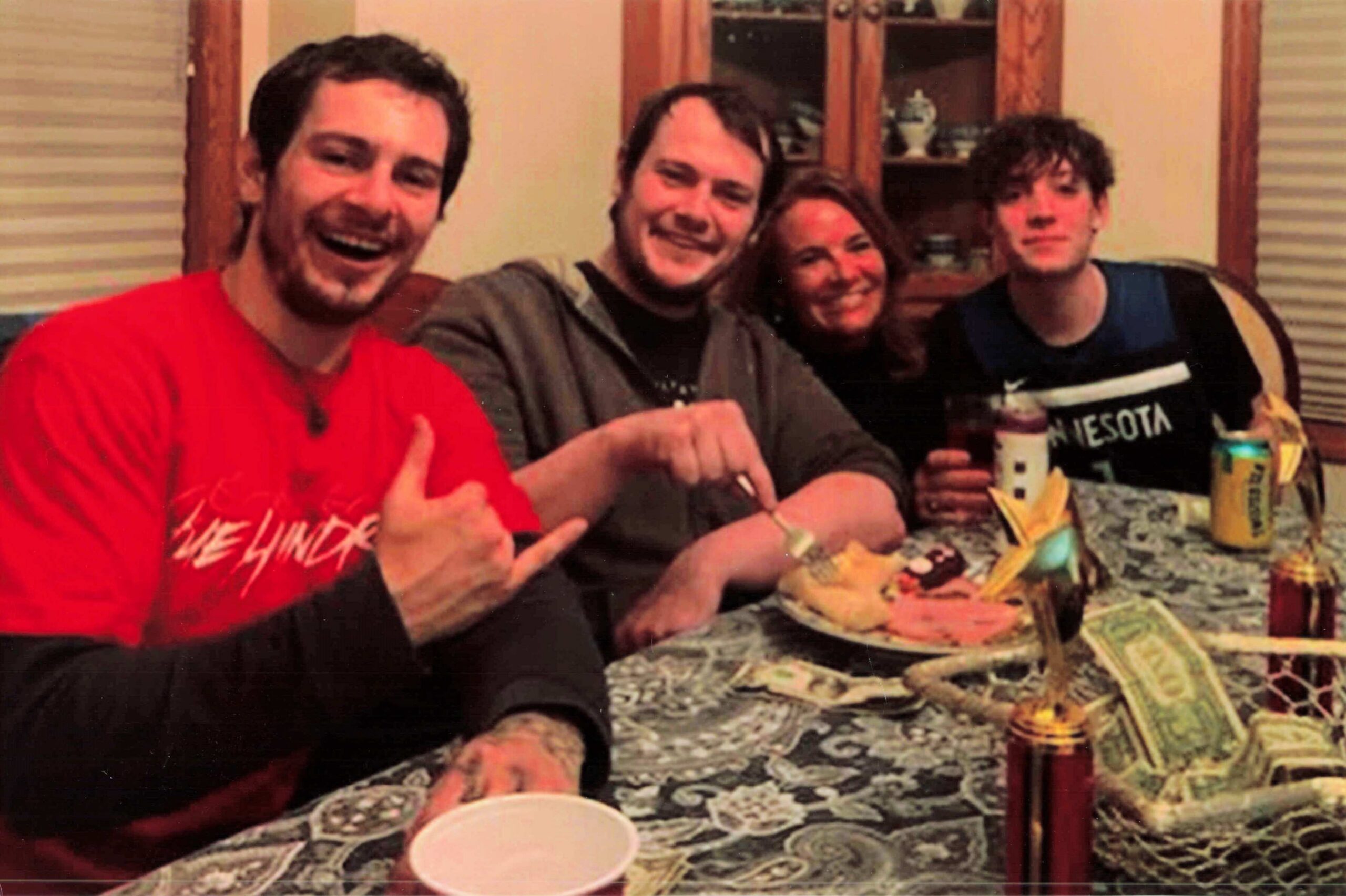Four friends sit together at a dining table, smiling for a casual group photo with drinks and snacks around them.