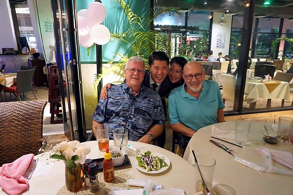 Four people posing at a restaurant table, two older men in front with two younger adults behind, smiling at the camera.