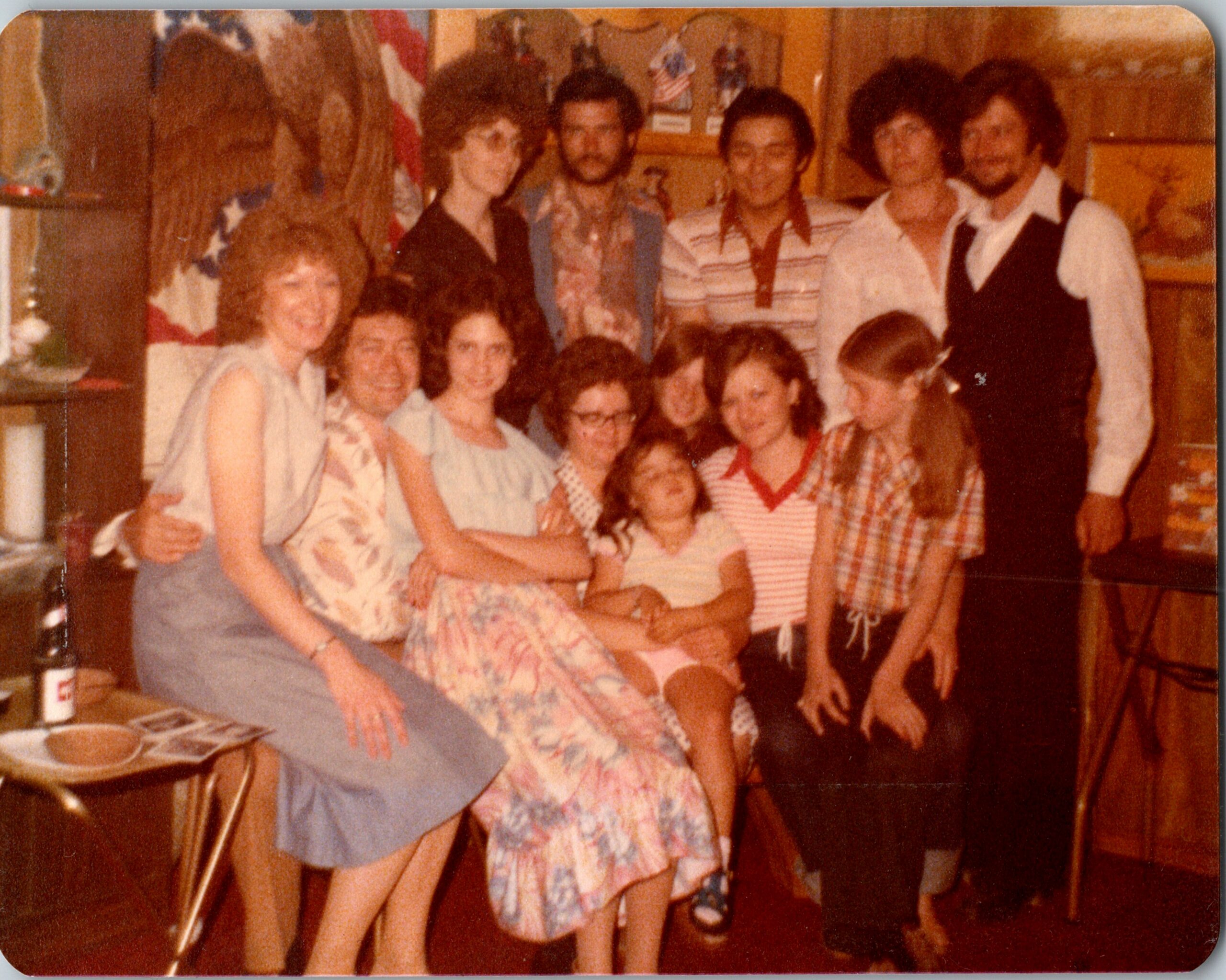 Group of people in 1970s attire posing together indoors, smiling for a casual photo at a party or gathering