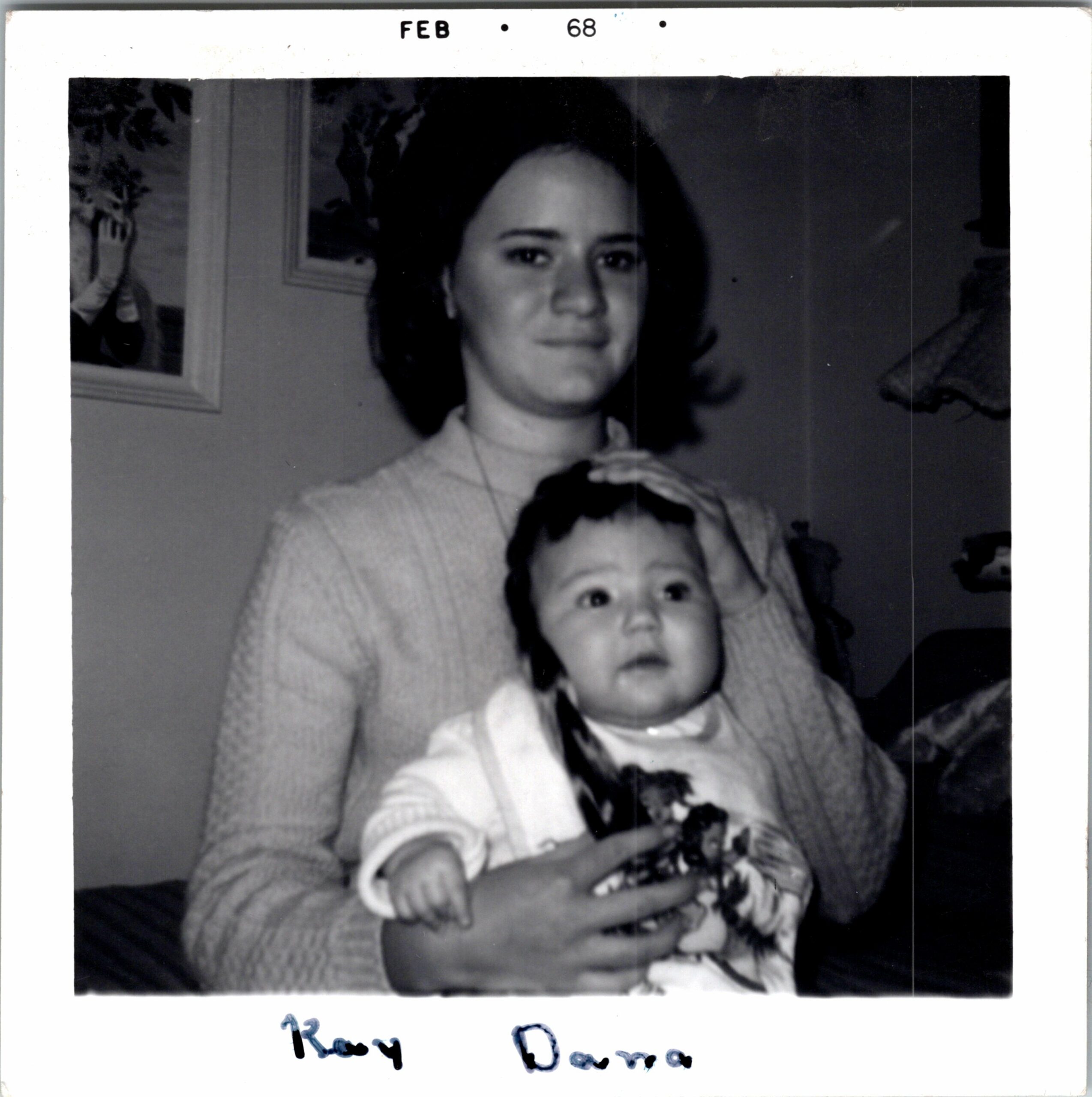 Black-and-white photo of a woman with short dark hair sitting behind a young child, both wearing light sweaters indoors.
