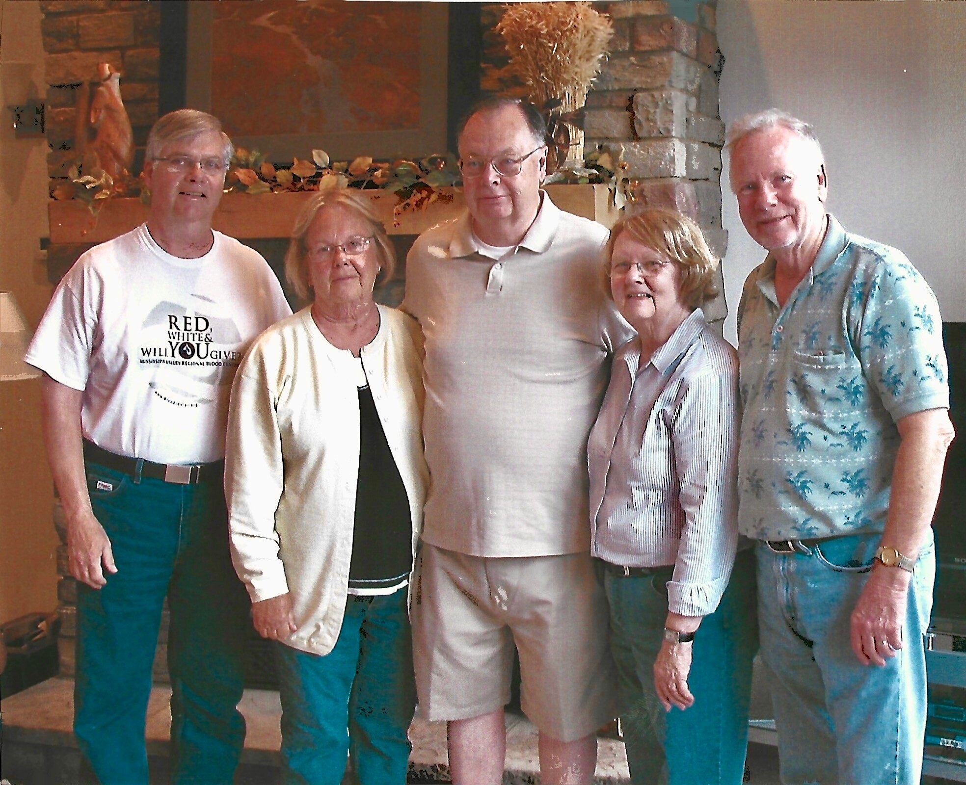 Five adults posing for a photo indoors in a living room with a stone fireplace behind them.