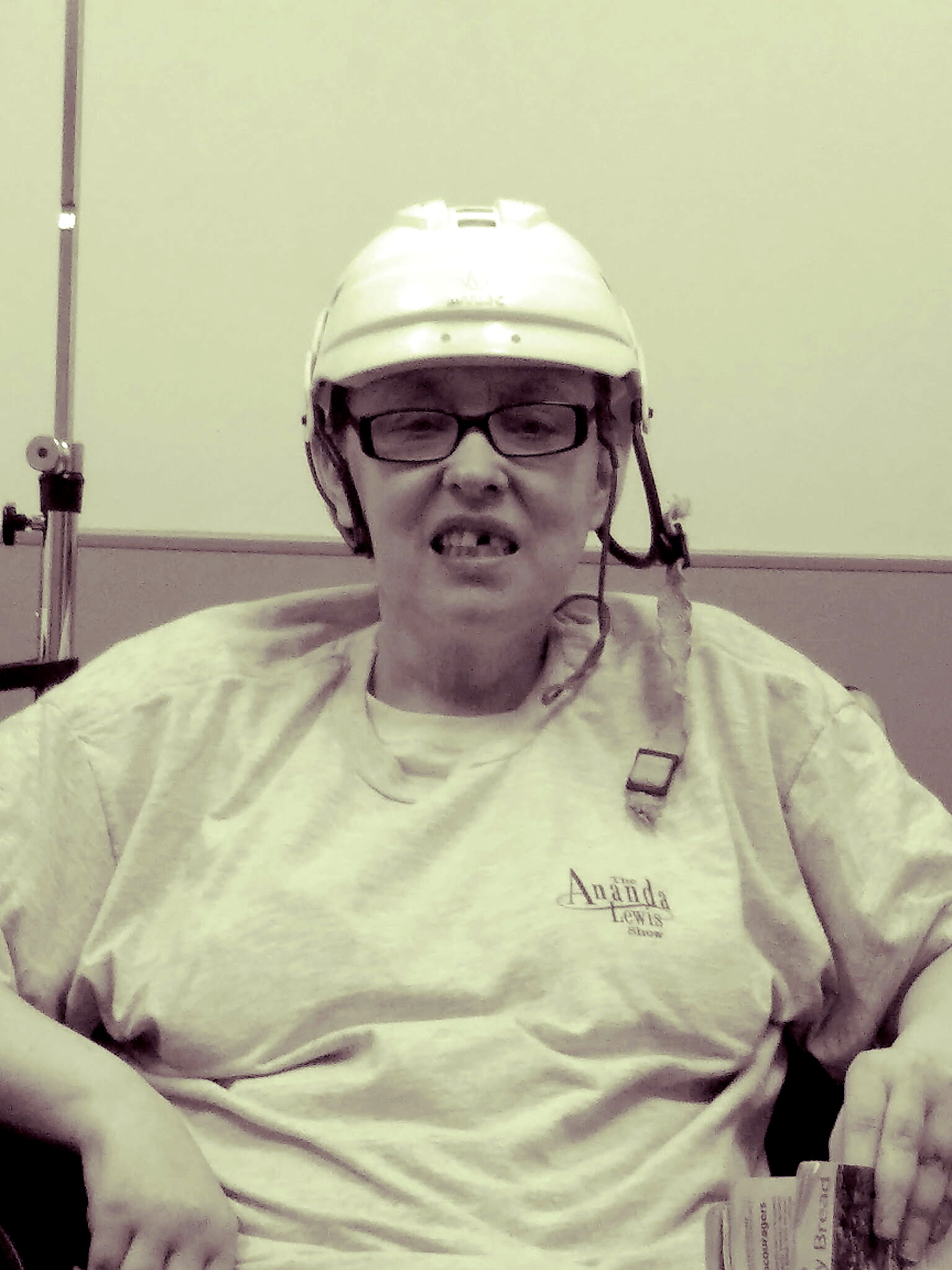Person wearing a white hard hat and glasses, speaking into a headset while seated in a light room.