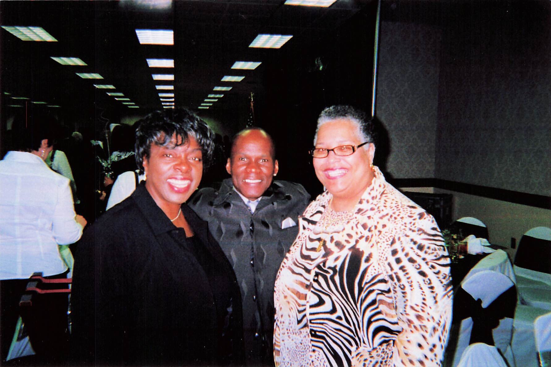 Three smiling adults posing together at a banquet hall reception.