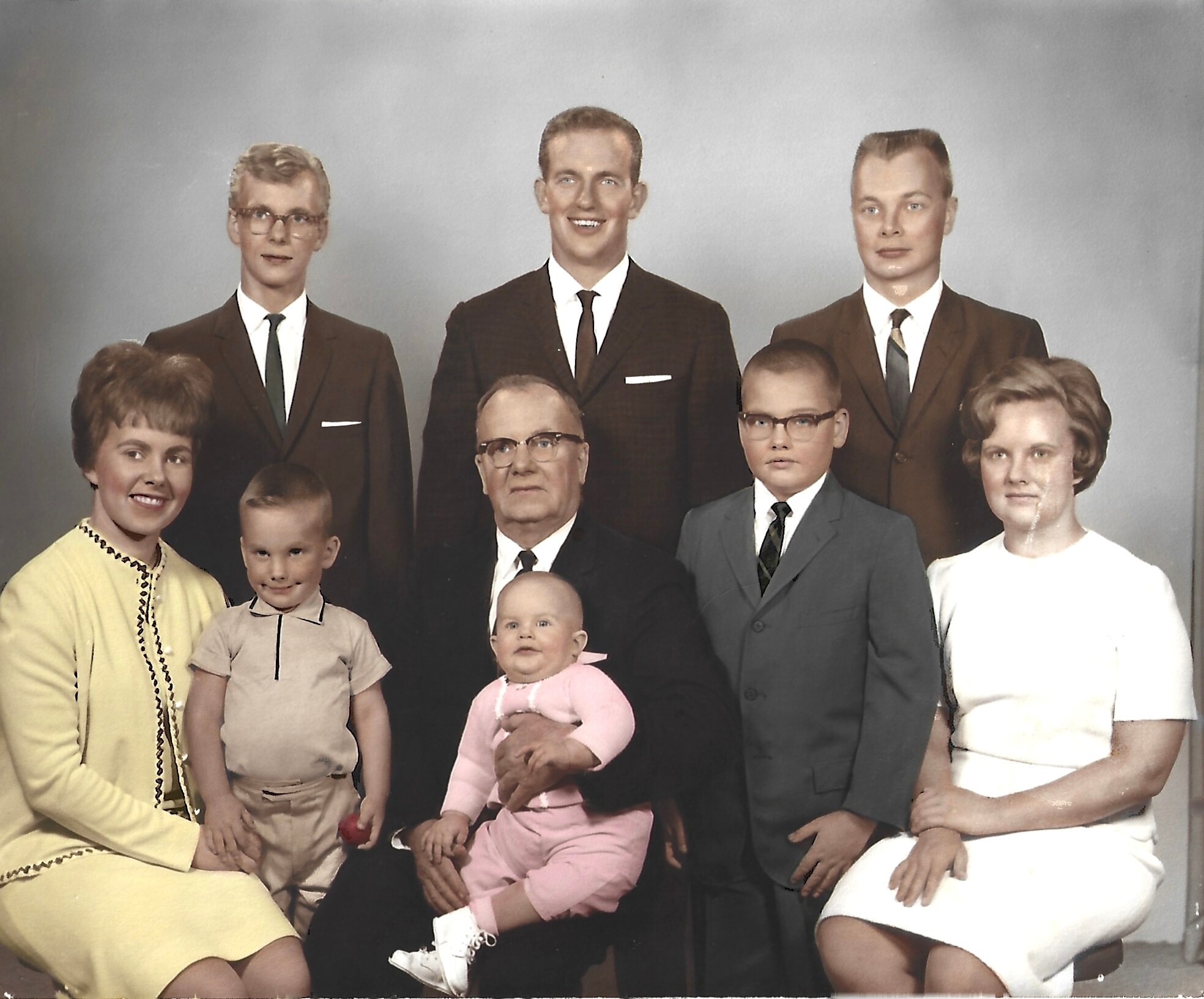 Family portrait of a multi-generation group in formal 1950s attire, with men in suits and women in dresses posing together in a studio setting.