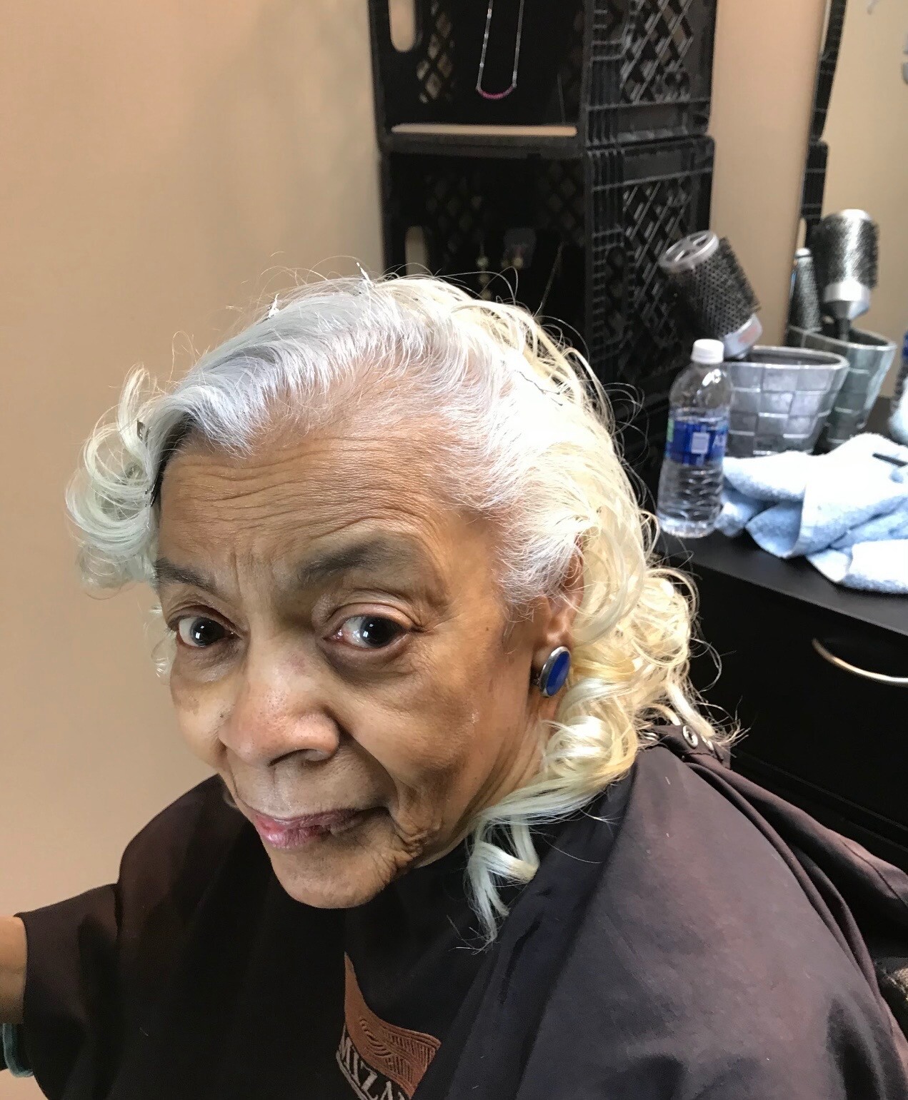 Close-up of an elderly woman with silver hair seated in a salon chair, wearing a dark cape during a haircut.