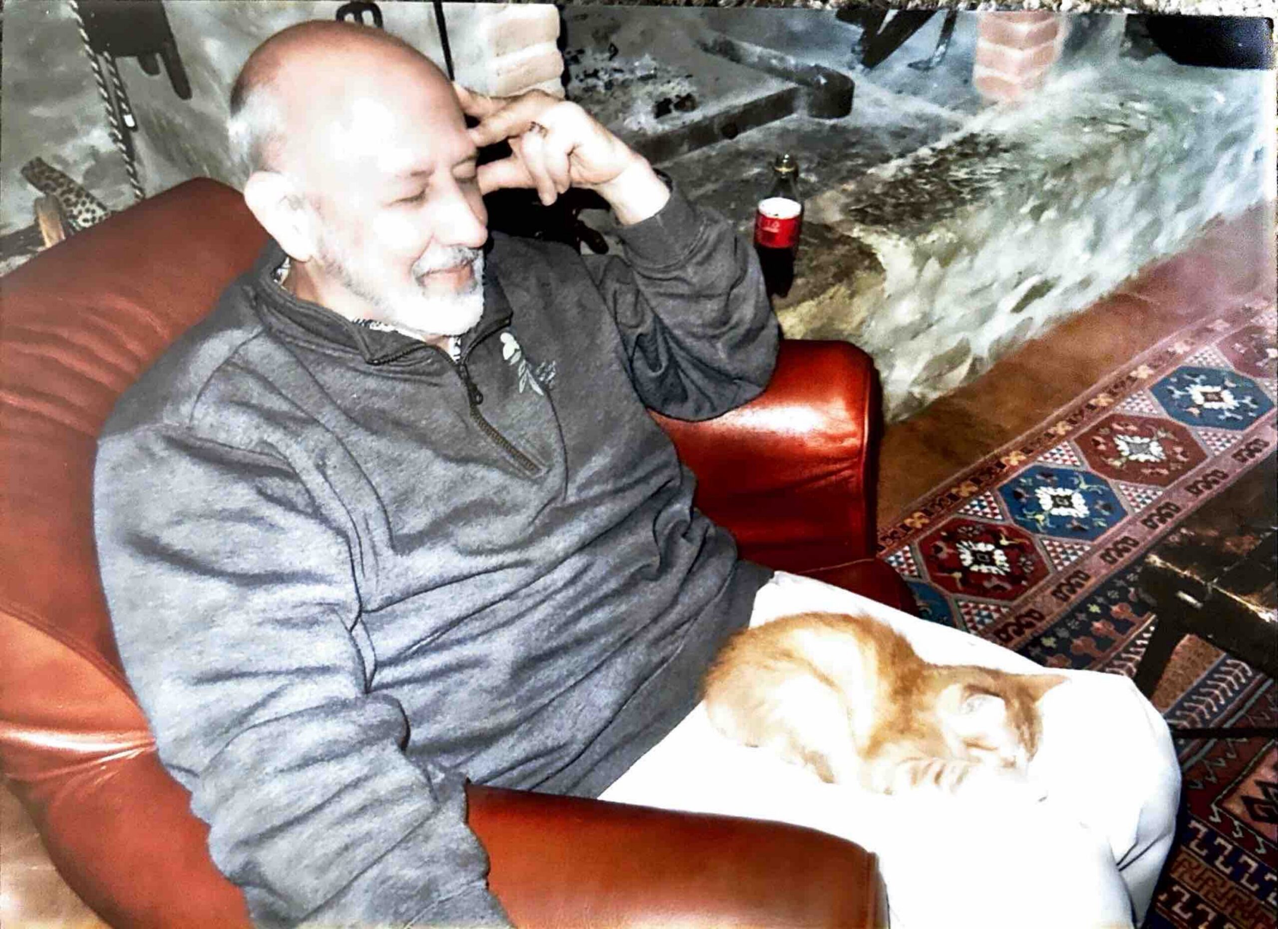 Older man with a white beard relaxing on a couch, a white dog curled up on his lap.