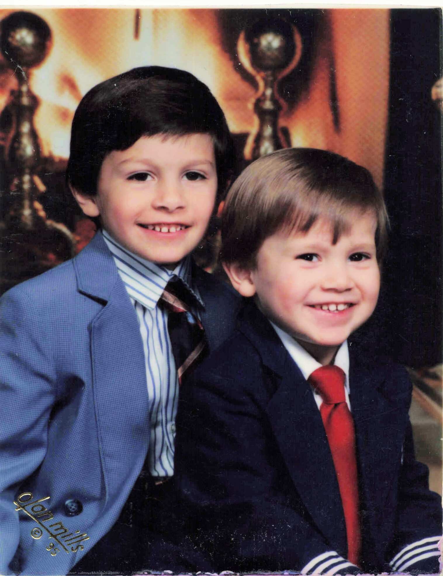 Two young boys in formal suits smiling for a family portrait.