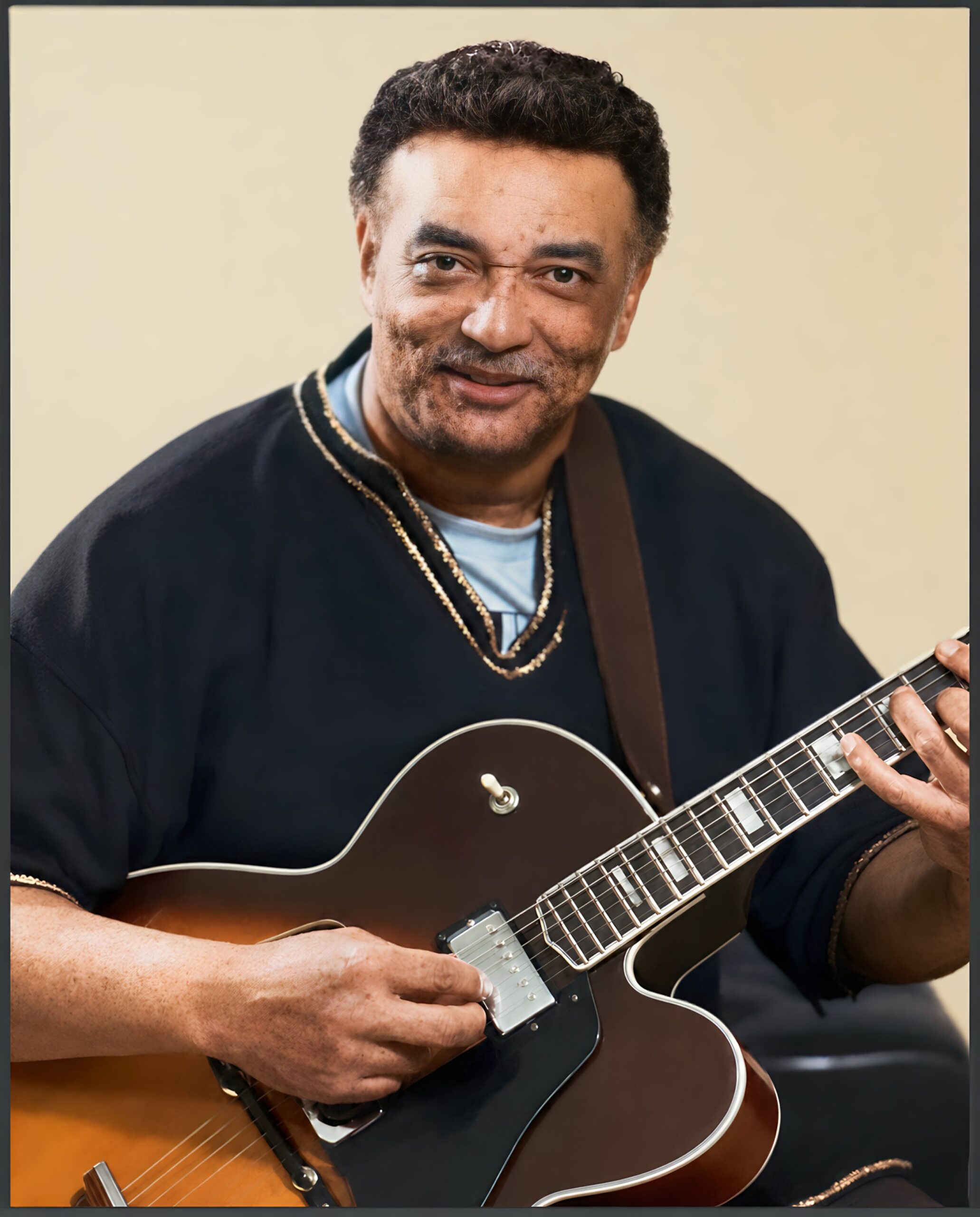 Man in a dark shirt playing a sunburst electric guitar, focusing on the fretboard and strumming with hands visible.