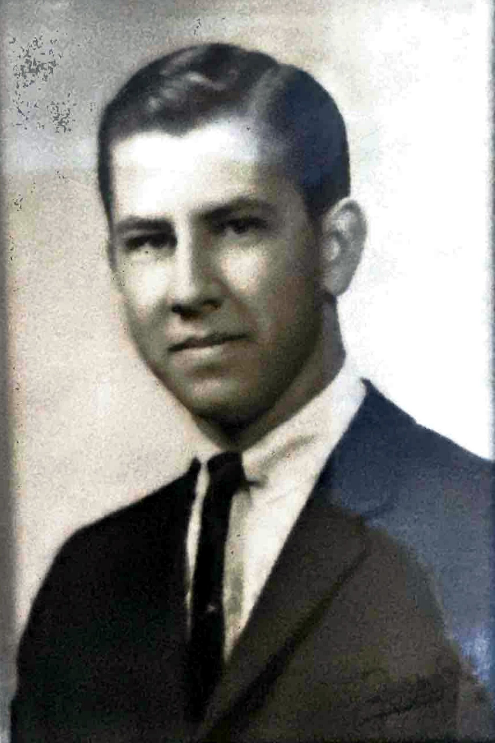 Black-and-white portrait of a man in a dark suit and tie, looking toward the camera.