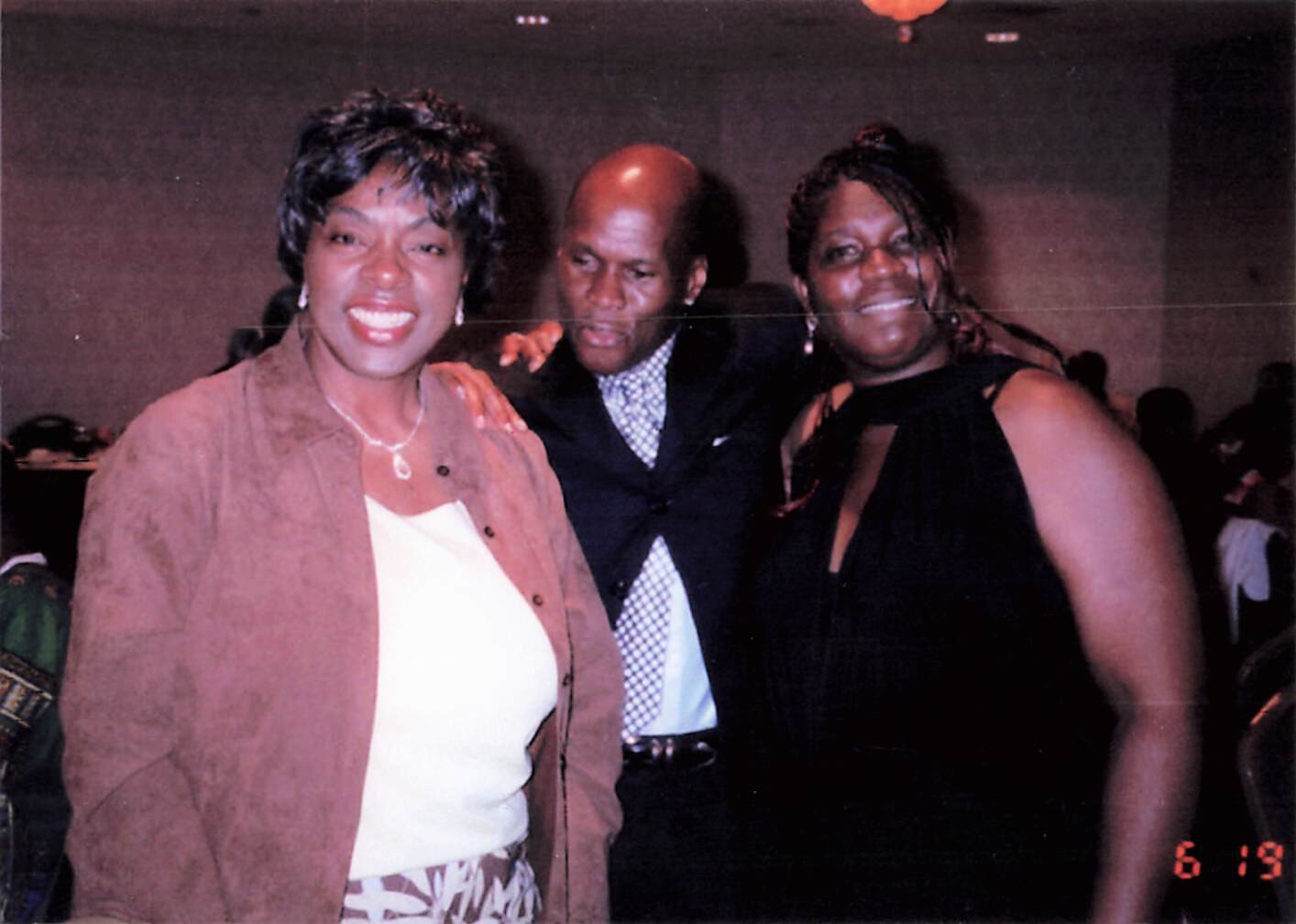 Three adults posing together at a social event, smiling for the camera with arms around each other.