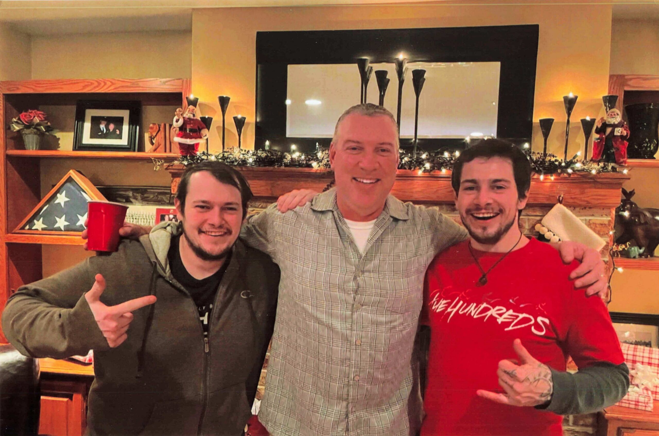 Three men posing together indoors, smiling with arms around each other, festive Christmas decorations in the background.