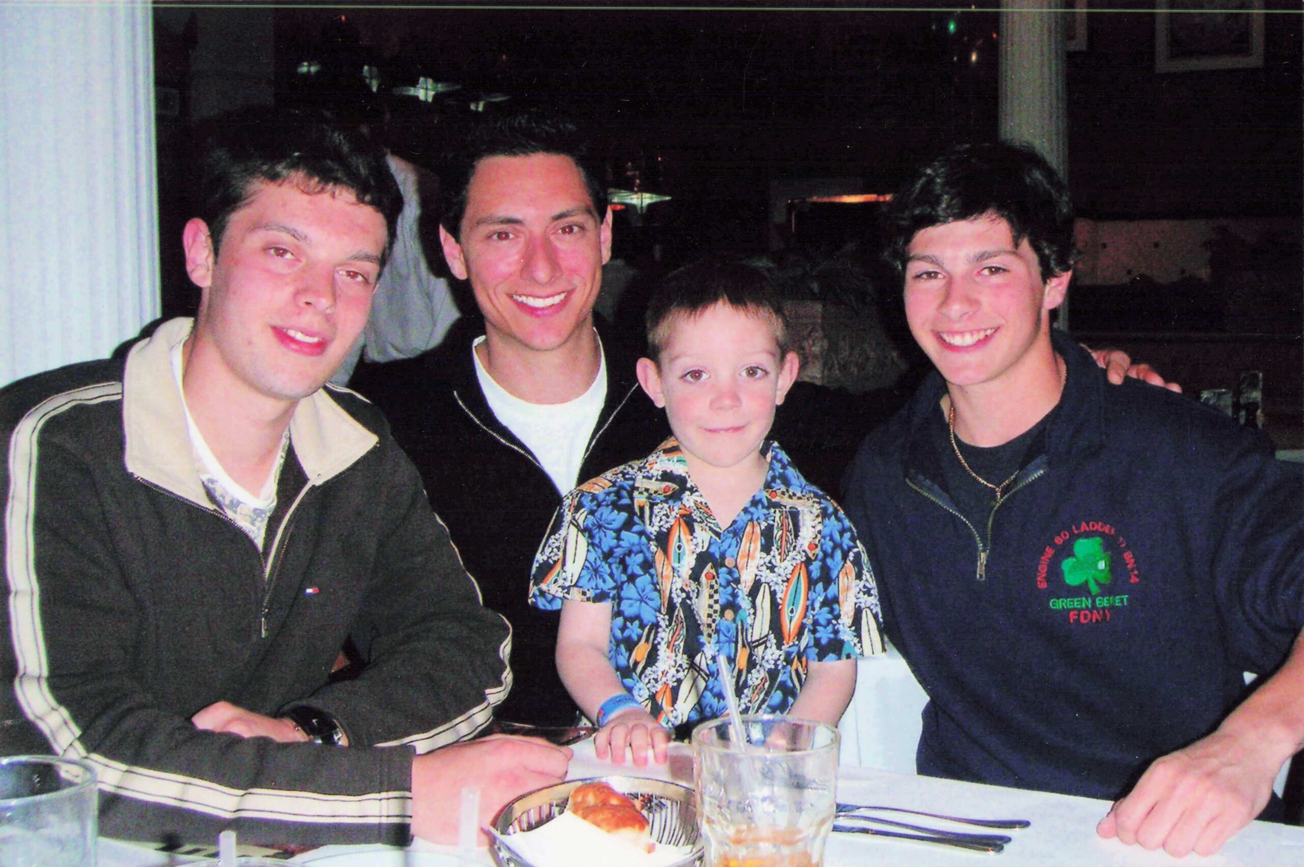 Group of four adults and a child posing together at a restaurant table, smiling for the camera.