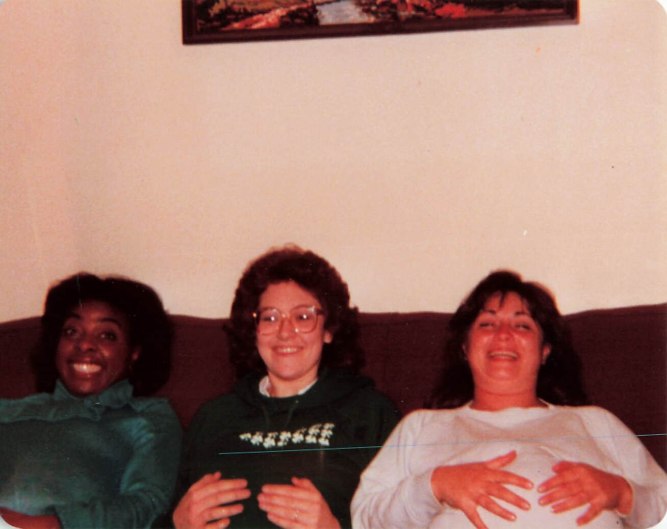 Three friends sit close together on a brown couch, smiling at the camera.
