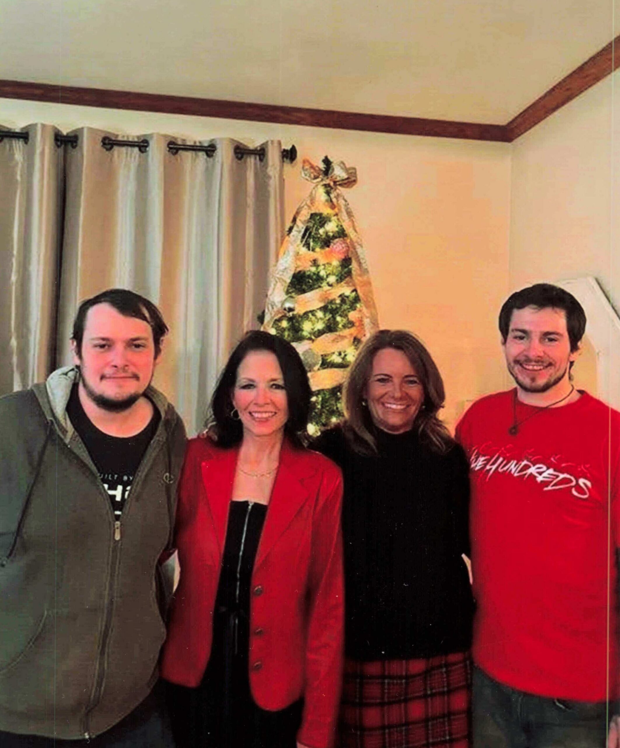 Group of five adults smiling for a holiday photo indoors, with a decorated Christmas tree visible behind them.