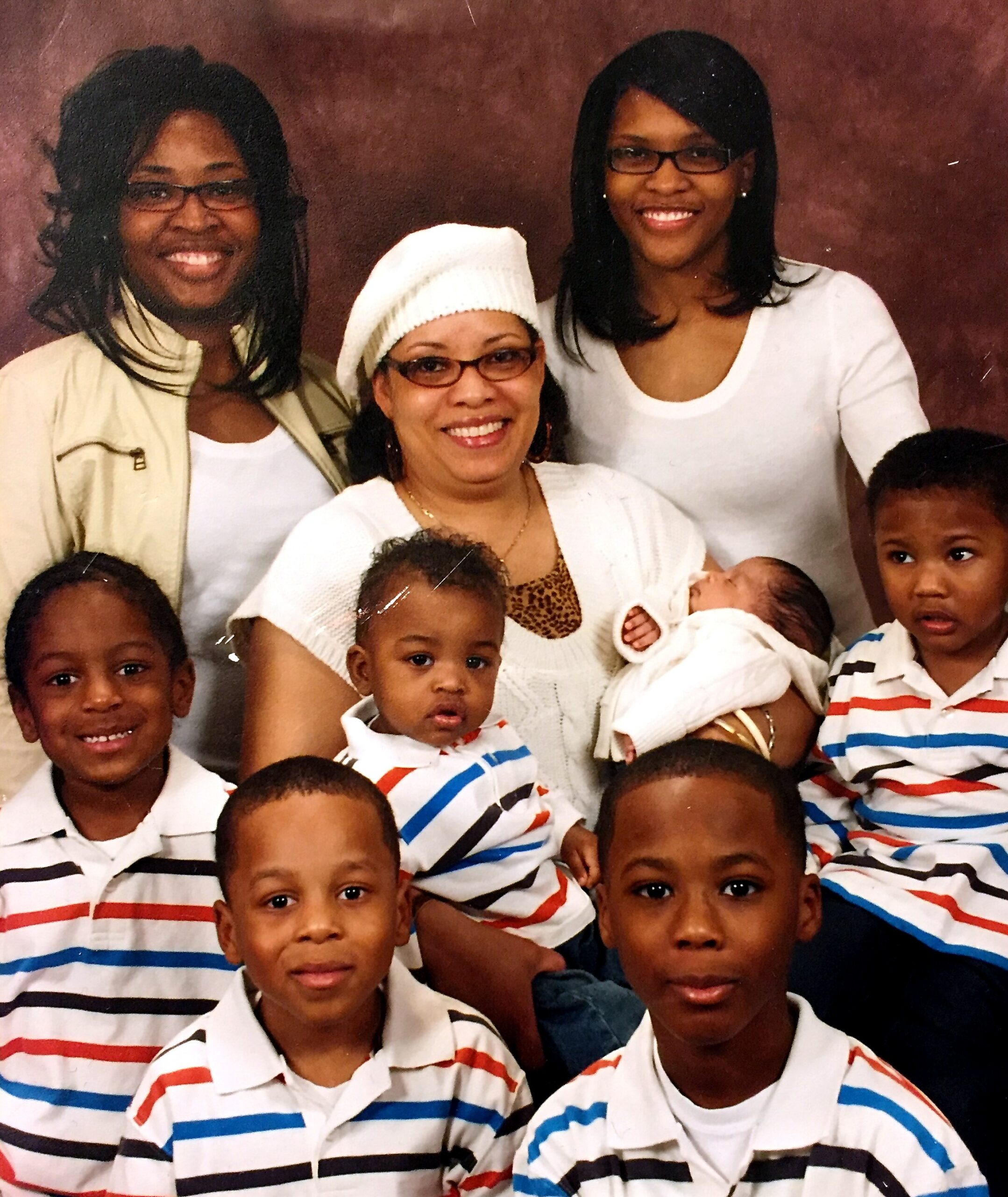 Group portrait of a smiling woman in a white hat with several children in striped shirts around her.