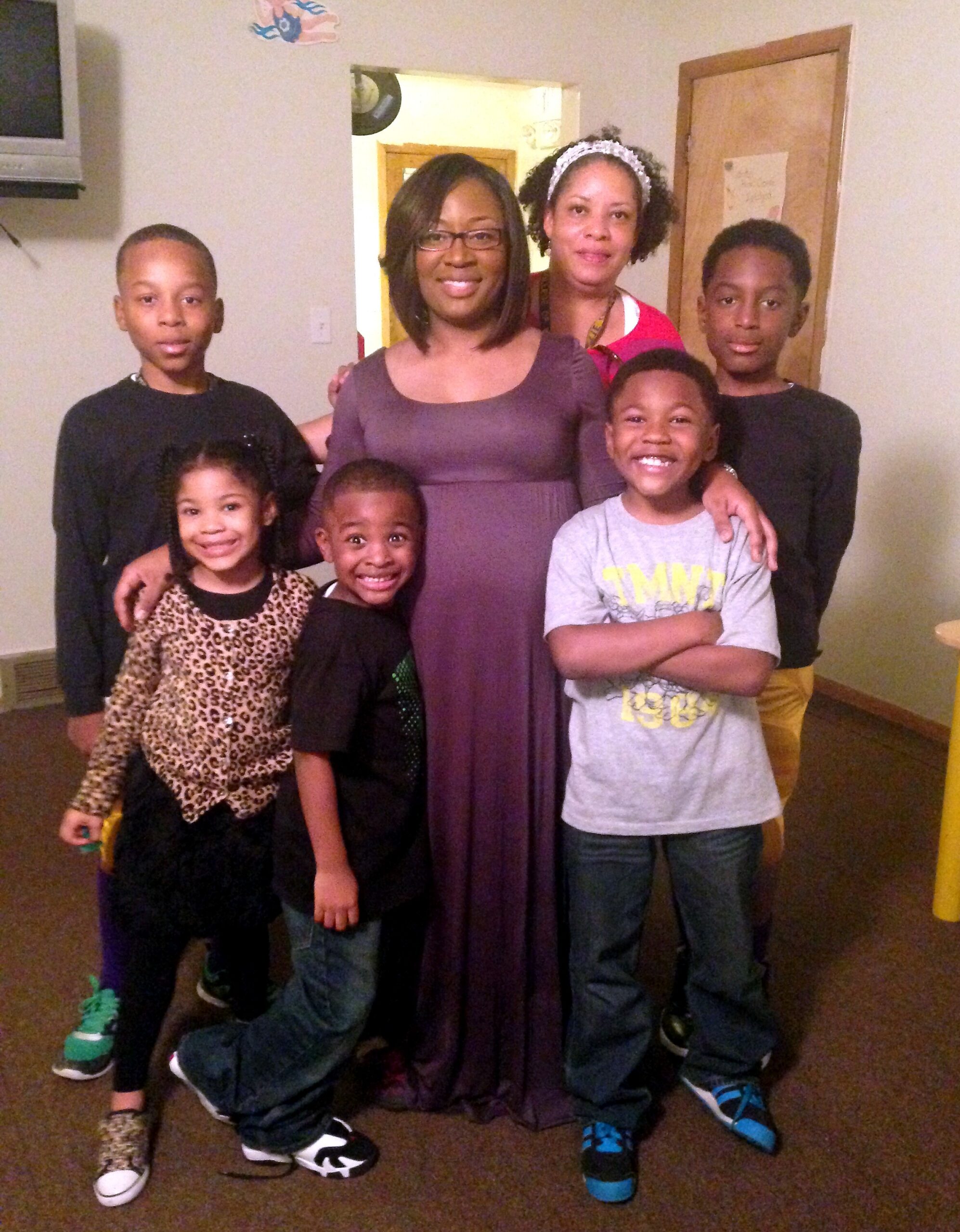 Group of eight family members posing together indoors, with two adults in the center and children around them, smiling in a living room.