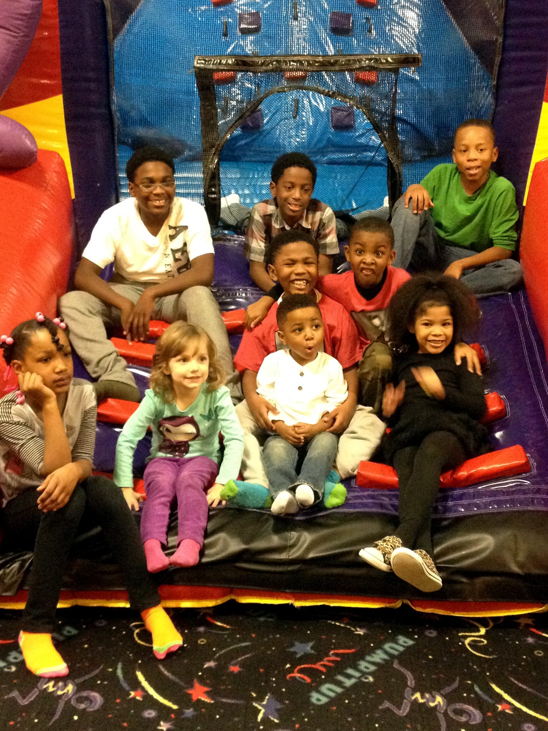 Group of smiling children sitting on a red inflatable slide inside a play area, posing for the photo.