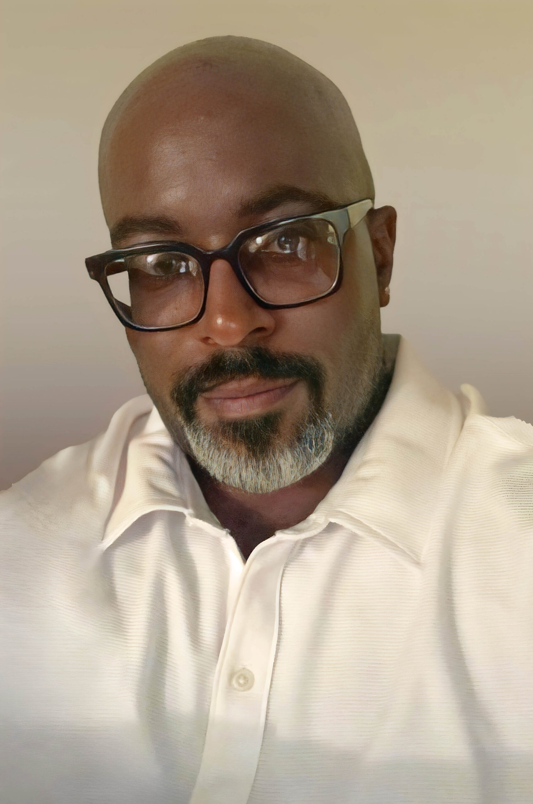 Close-up portrait of a bald man wearing black-framed glasses and a white polo shirt, looking at the camera.