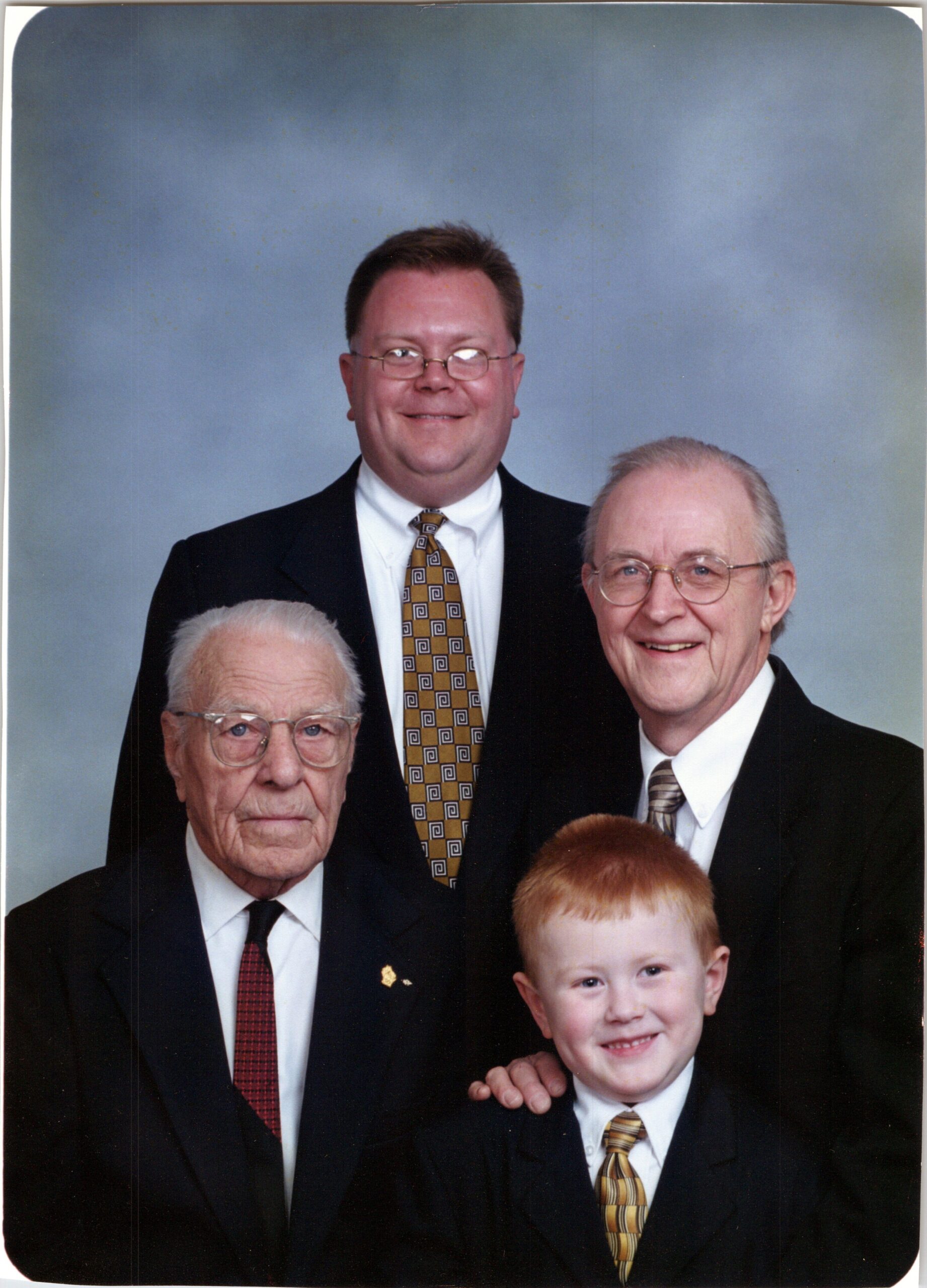 Group portrait of three men in suits with a smiling child in front, against a blue backdrop.