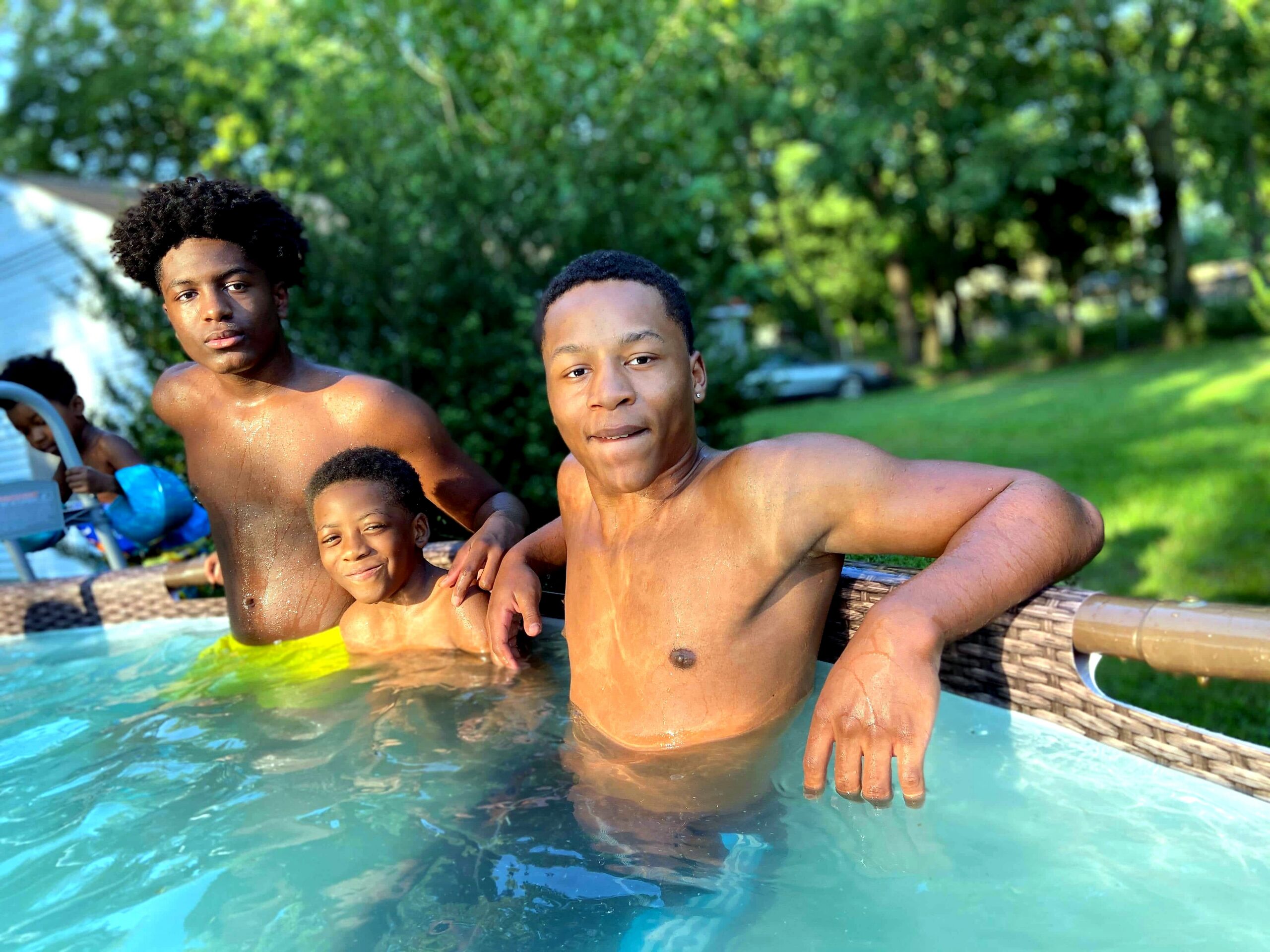 Group of shirtless boys posing at the edge of a pool with a green backyard behind them.
