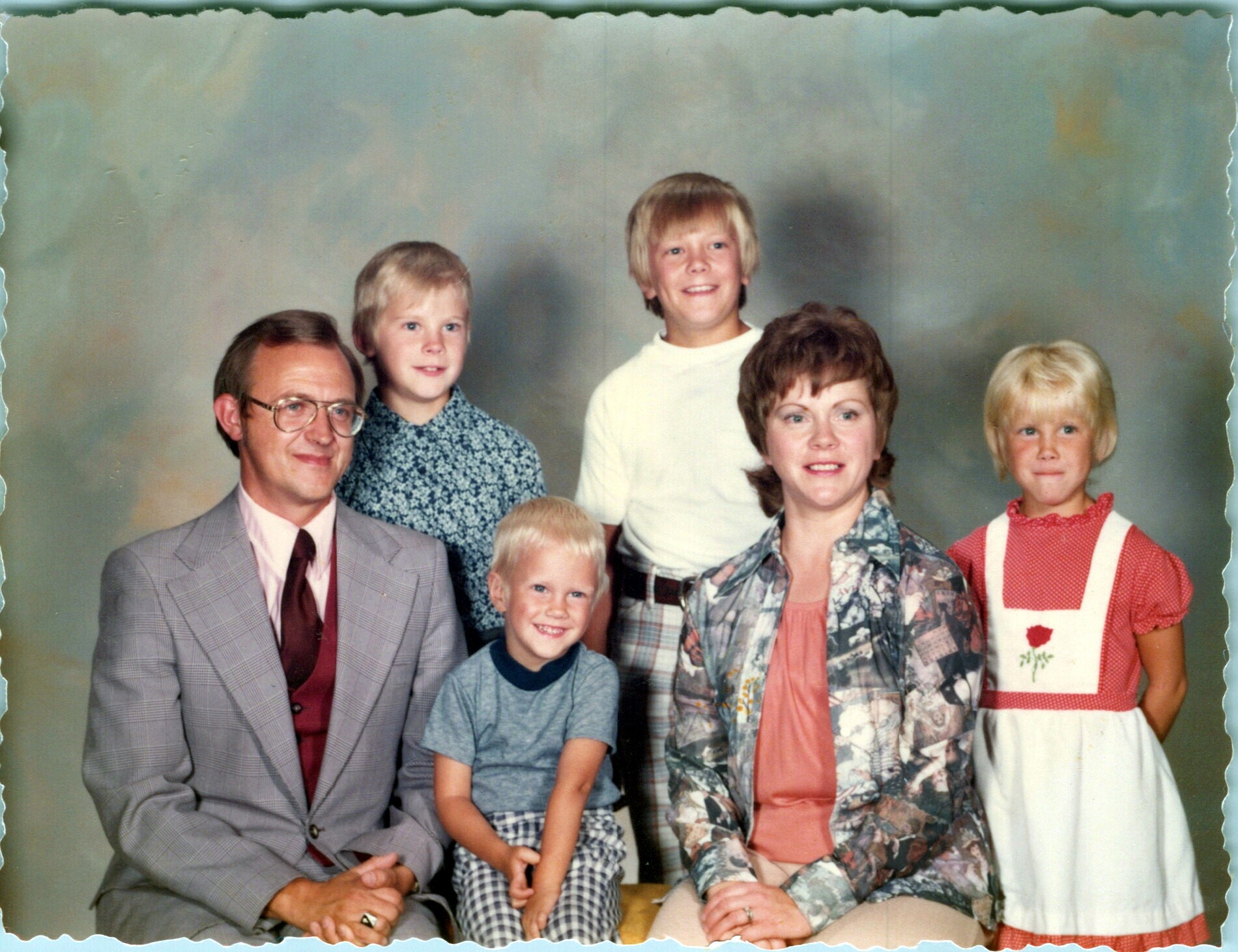 Family portrait of two adults and several children posing in a studio with soft backdrop, all smiling.