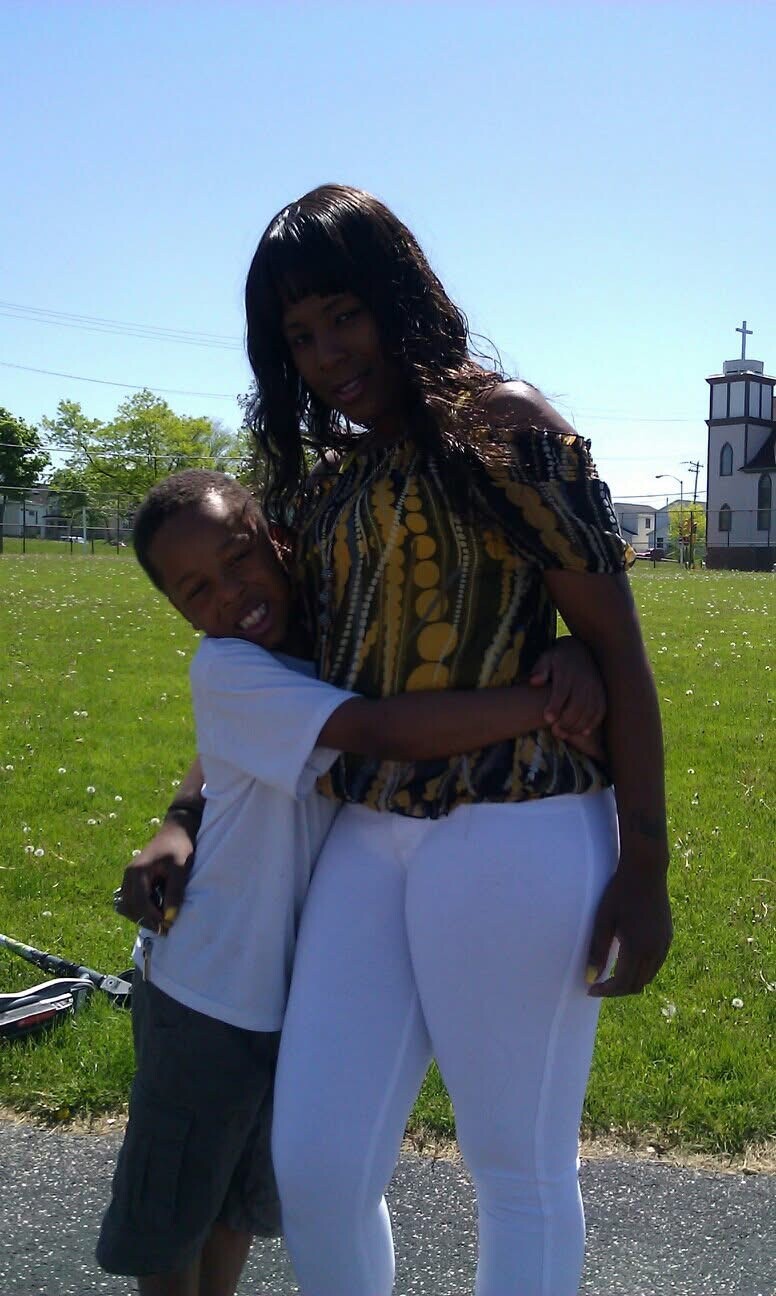 Woman and young boy sharing a hug in a sunny park, with a church in the distance behind them.