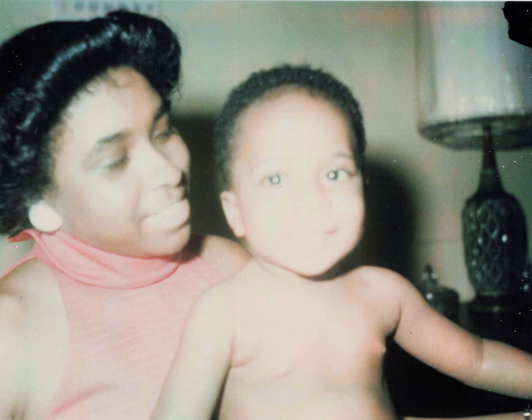 Two babies close together in a soft-focus photo, with one wearing a pink outfit; cheerful, cropped close-up portrait.