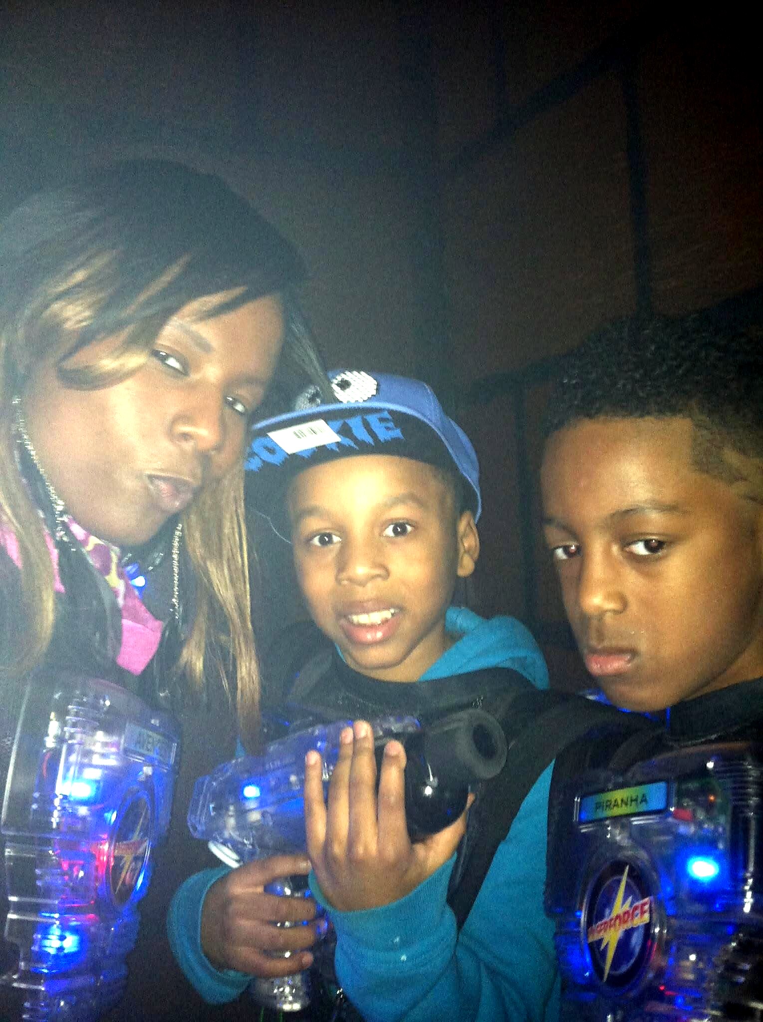 Family selfie inside a transparent vehicle at night: a woman on the left making a kissy face, and two boys in the middle and right, with blue lights in the background.