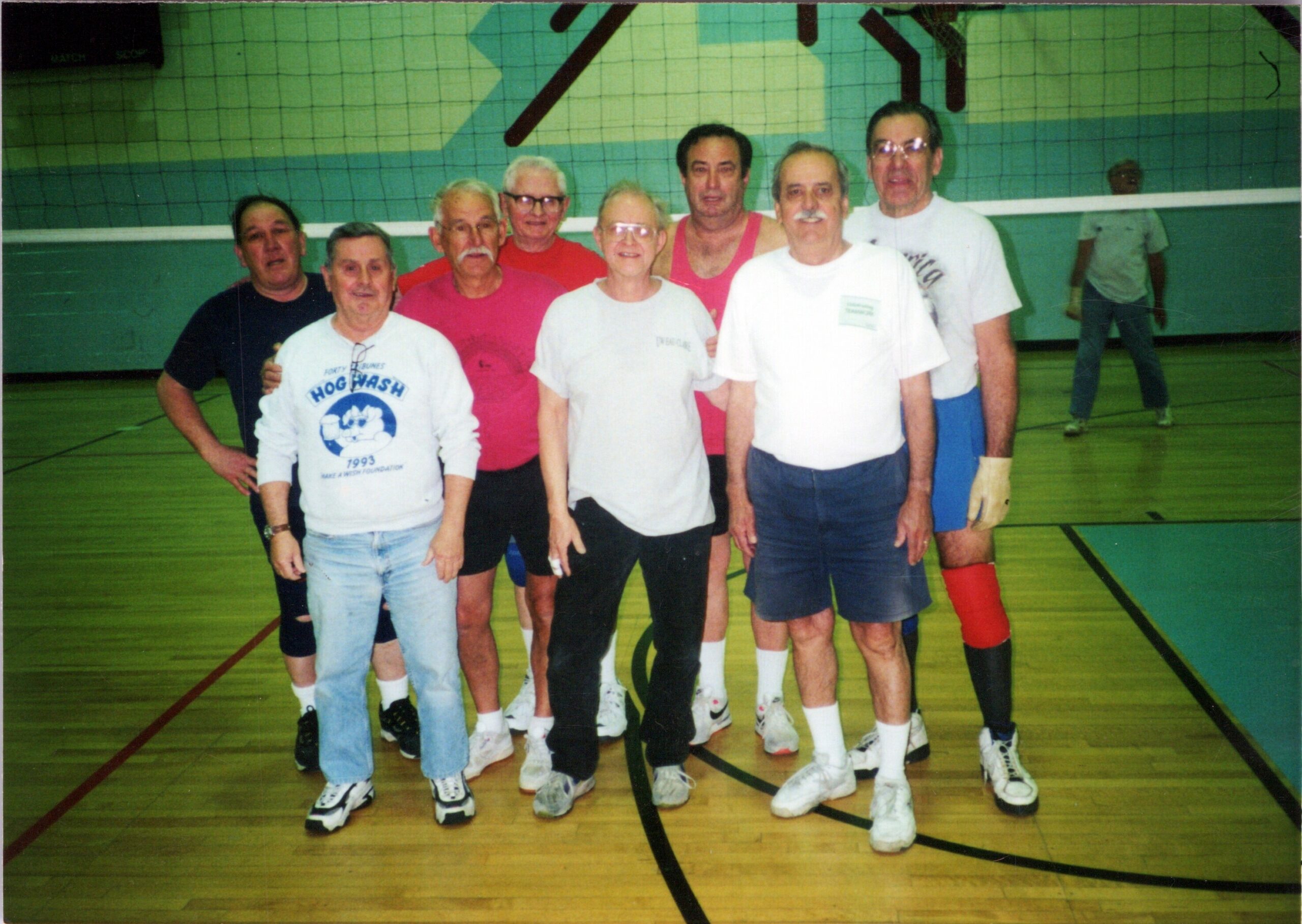 Group of older adults in a gym posing for a photo after a game, wearing sports shirts and shorts.