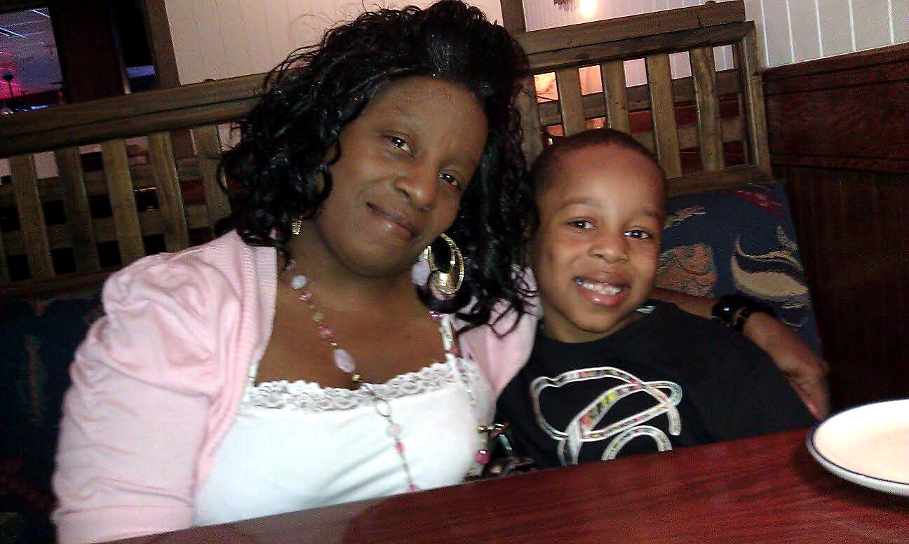 Woman and young boy smiling at a restaurant table, seated close together in a booth with a plate visible on the table.