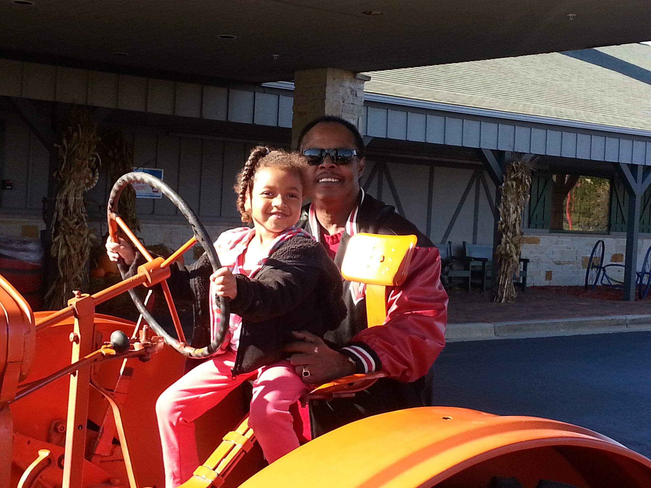 Adult wearing sunglasses holding a smiling child on an orange amusement ride outdoors.