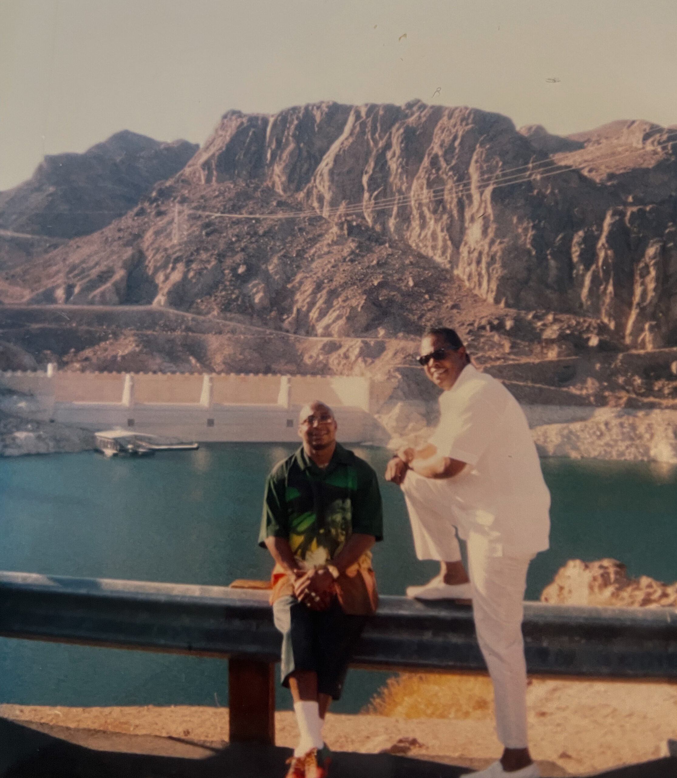 Two men posing by a turquoise pool with rugged rocky cliffs rising behind them.