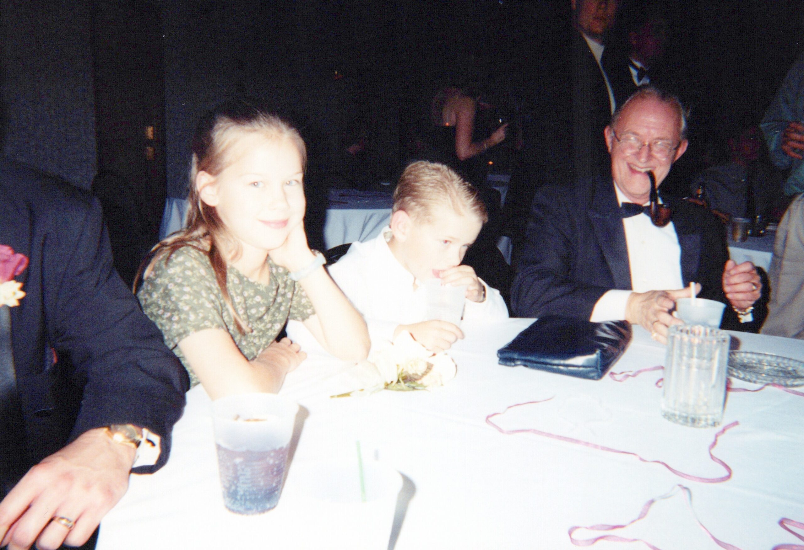 People sit at a banquet table during a formal event, with drinks and ribbons visible on the table.