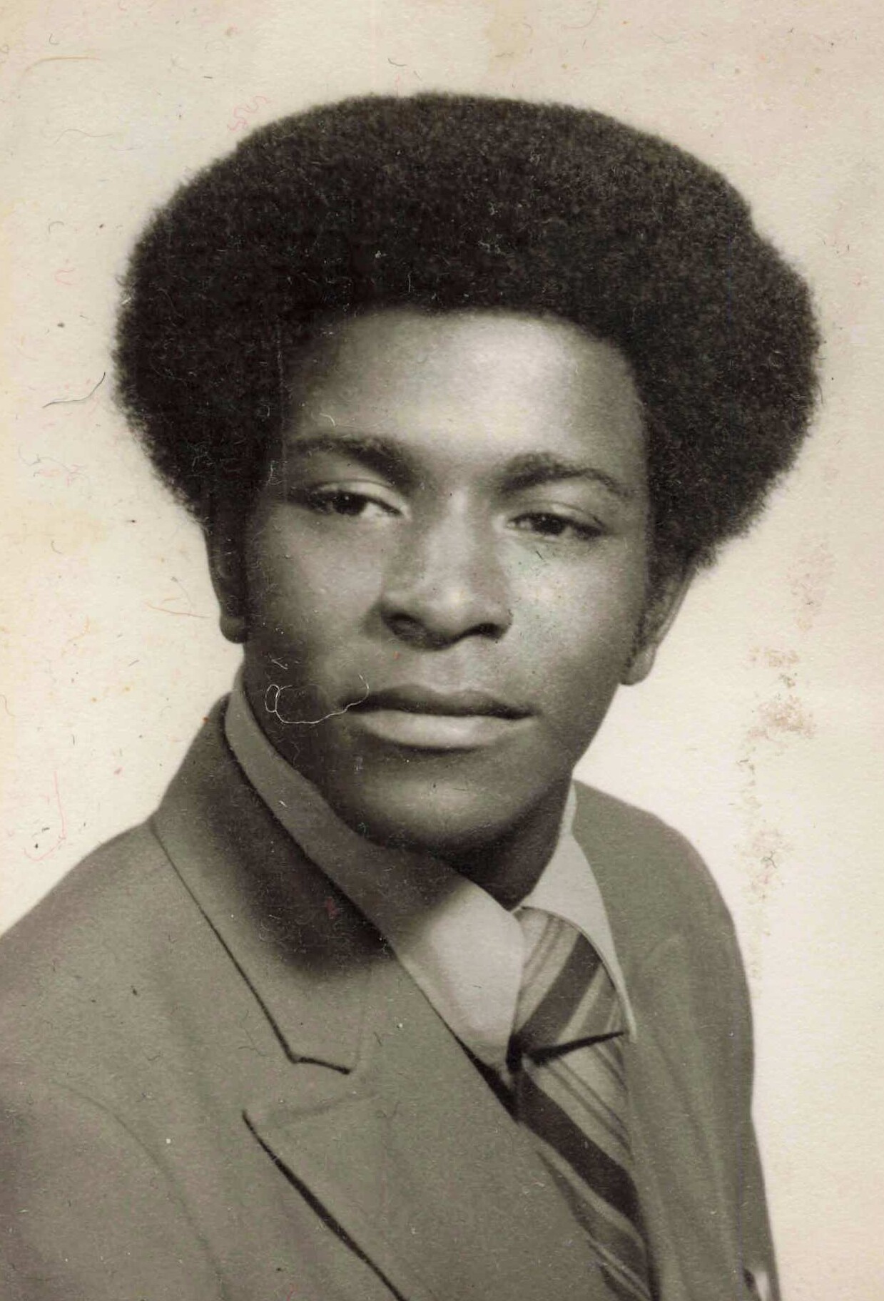 Young man in a suit and striped tie, posed studio portrait with a large afro hairstyle.