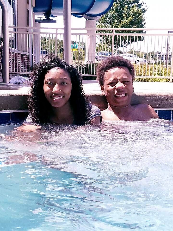 Two people smiling while leaning on the pool edge on a sunny day by a water slide.