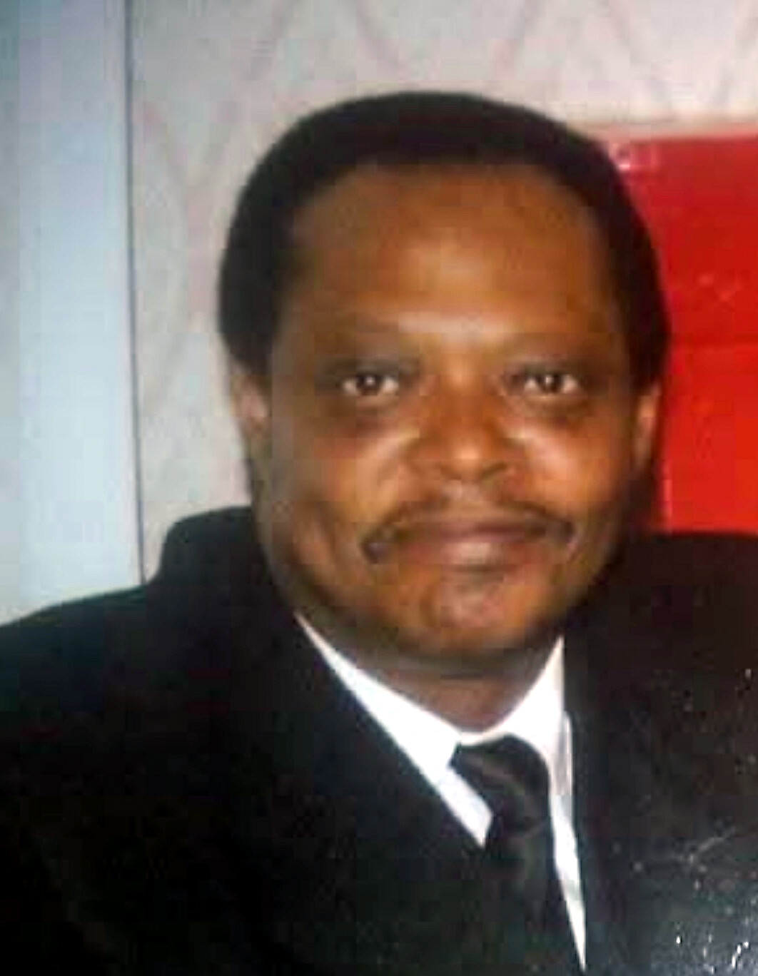 Smiling man in a dark suit and white shirt, shoulders visible, posing for a formal photo.