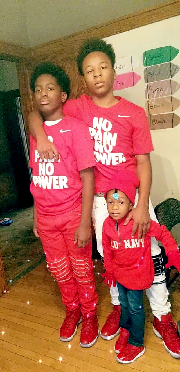 Three siblings pose indoors in matching red outfits; two teens wear 'NO PAIN NO POWER' shirts and a toddler in a red zip hoodie.