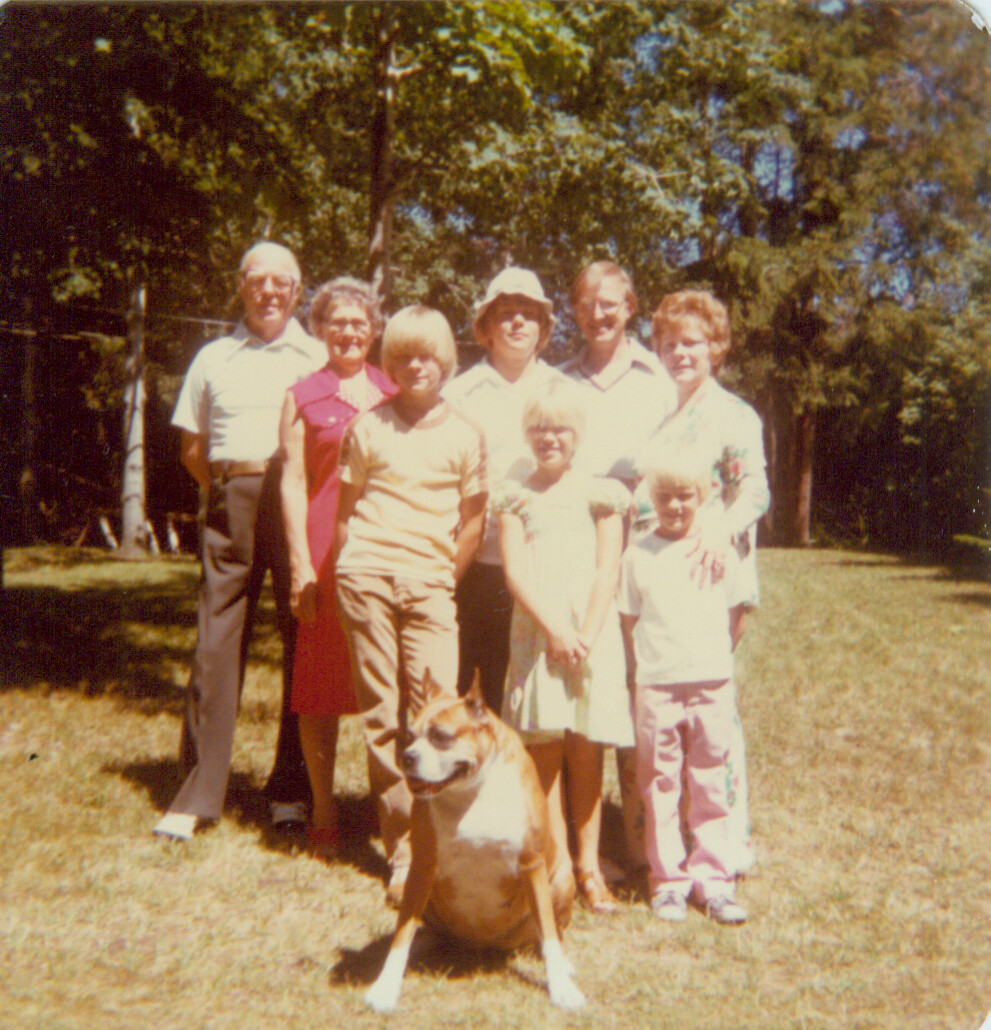 Family group outdoors posing for a photo with a brown-and-white dog at the front.