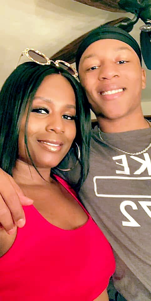 Smiling couple posing for a selfie indoors; woman in a bright pink top, man in a gray shirt with a headband.