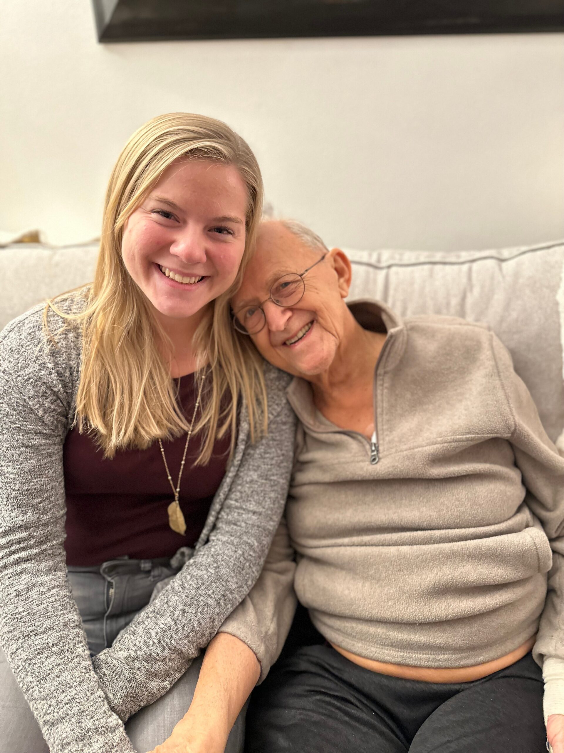 Smiling young woman and elderly woman sitting close together on a sofa.
