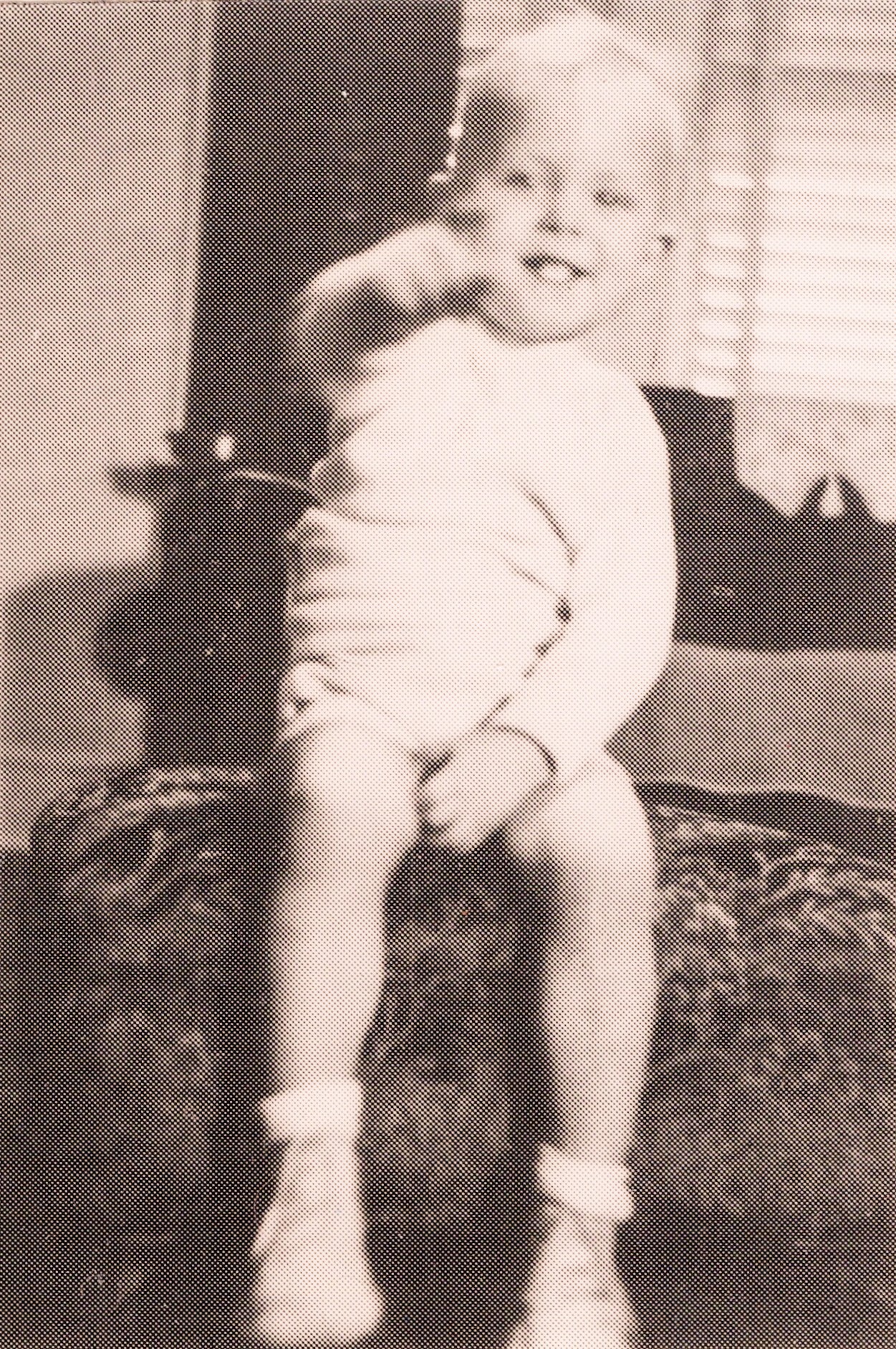 Baby standing outdoors, reaching forward with both arms, wearing a diaper and socks on a grassy yard.