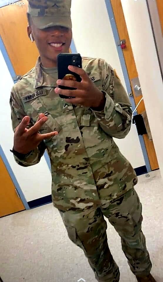 Soldier in camouflage uniform taking a mirror selfie, smiling and flashing a peace sign.