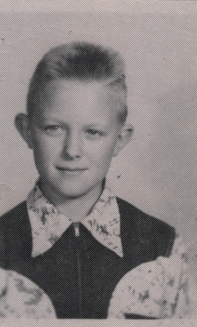 Black-and-white portrait of a smiling boy in a collared, patterned shirt and dark jacket.
