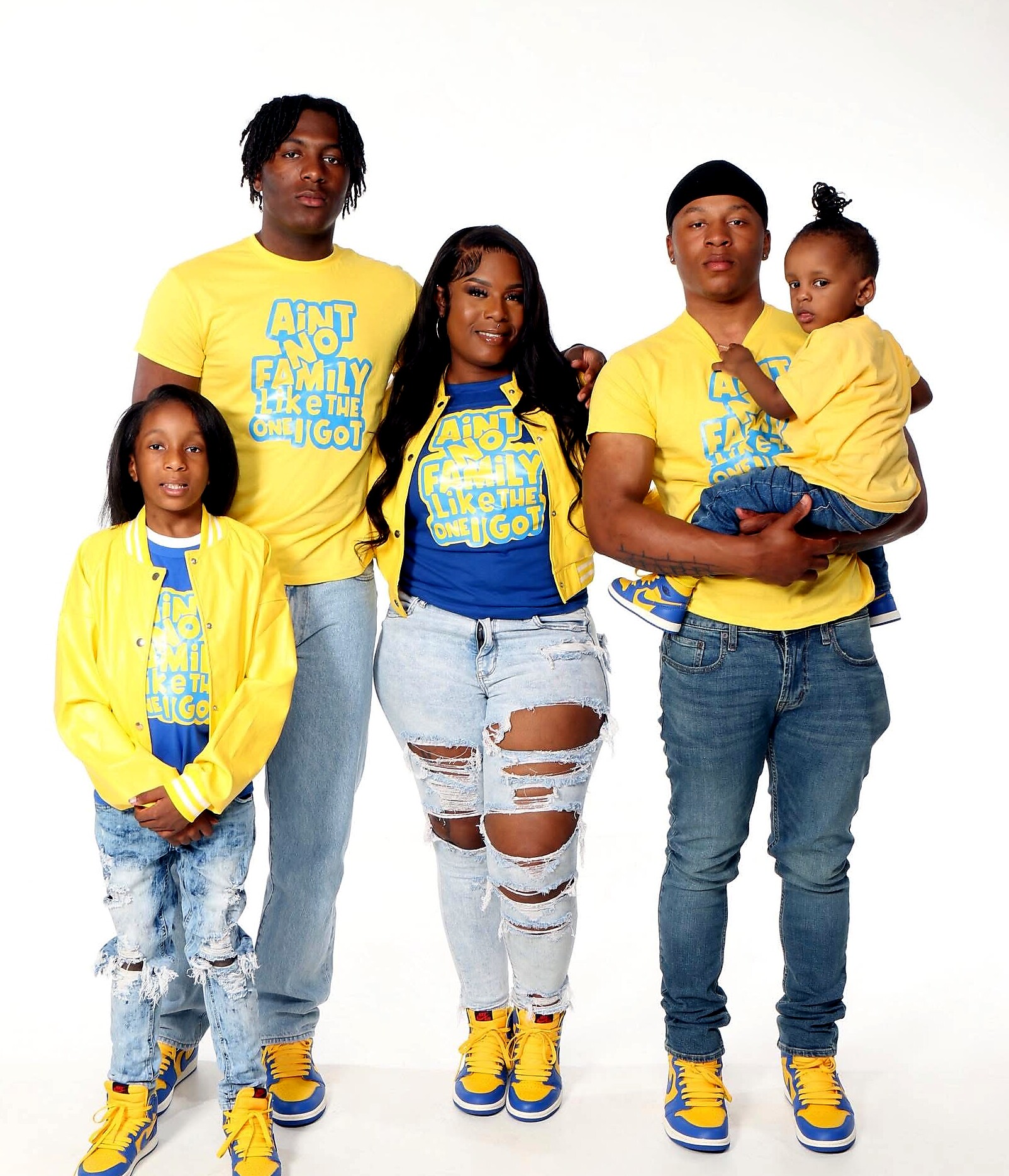 Family of four in matching yellow shirts with the slogan 'Ain't no family like the one I got', posing together in a studio.