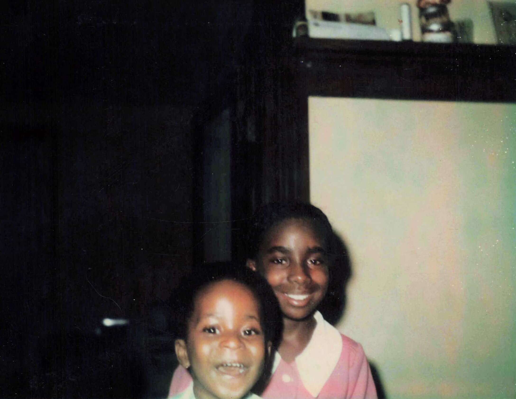 Three smiling children posing together for a group photo indoors, likely at school or home.