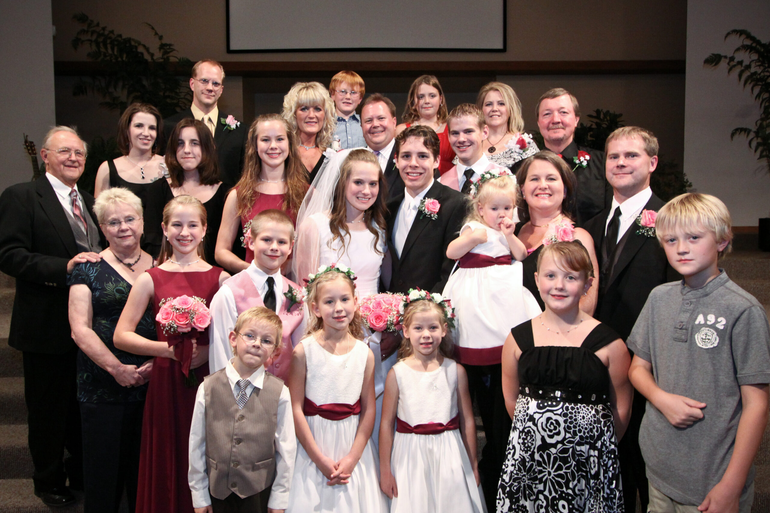 Group portrait at a wedding reception with bridesmaids, groomsmen, and family holding pink bouquets.