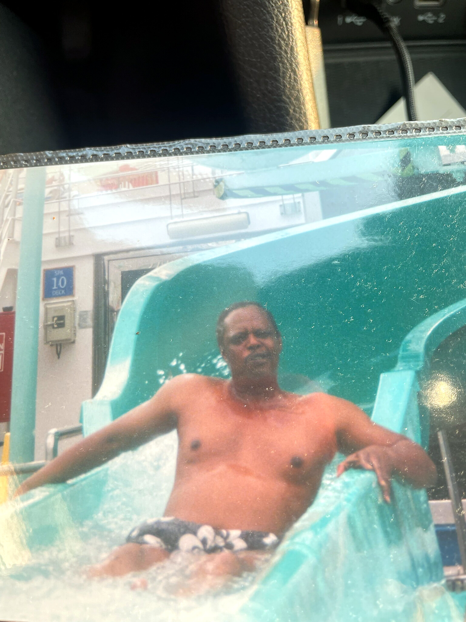Shirtless man seated in a turquoise water slide tub, facing the camera at a water park.