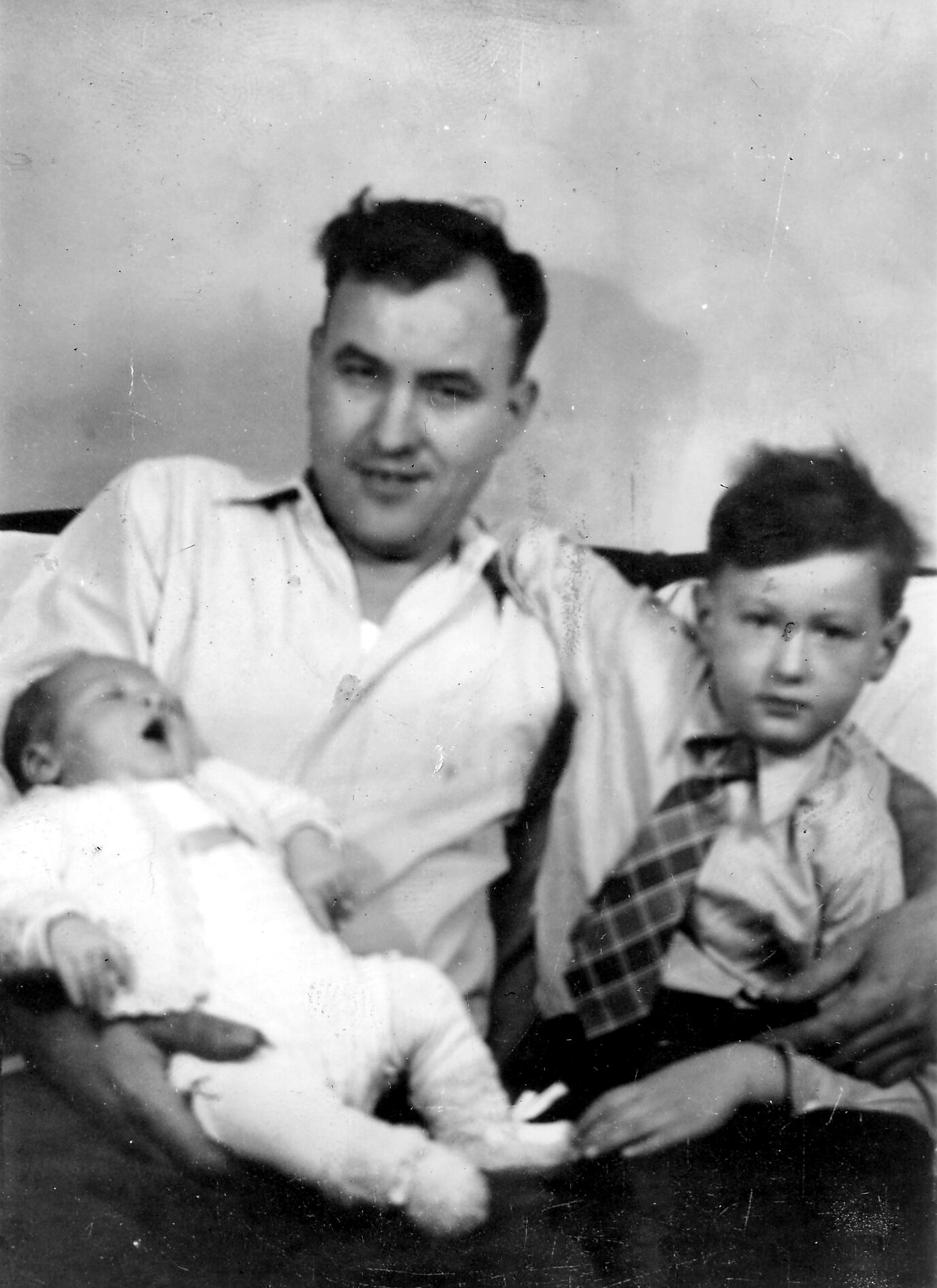 Man smiling with two young children on a couch; black-and-white family photo.
